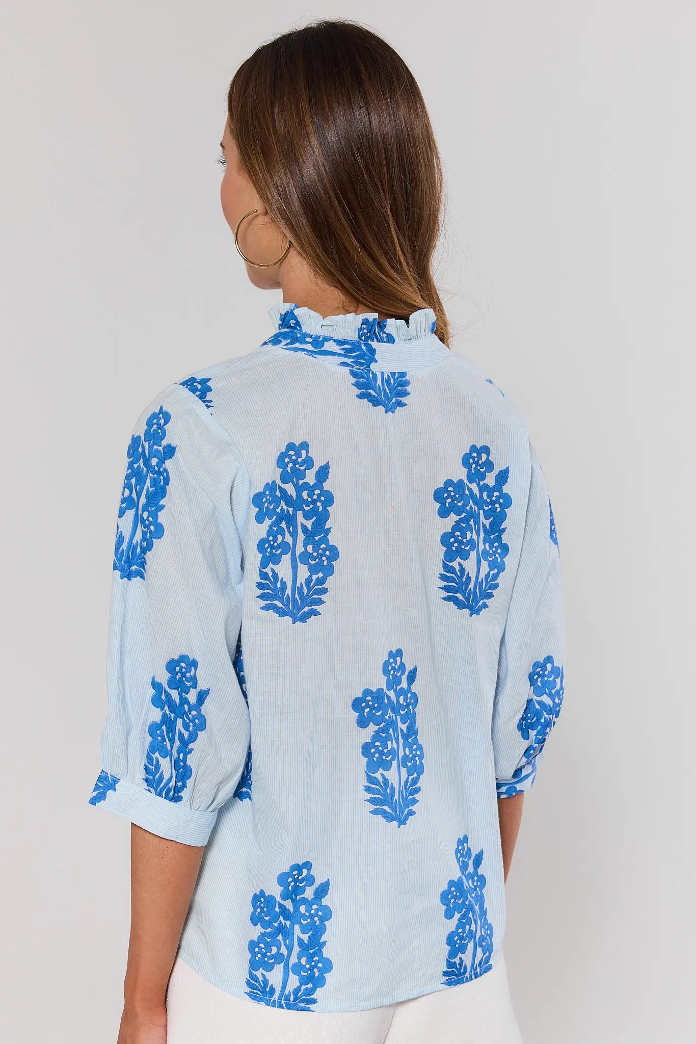 Woman standing wearing a light blue blouse with blue floral patterns on a plain background