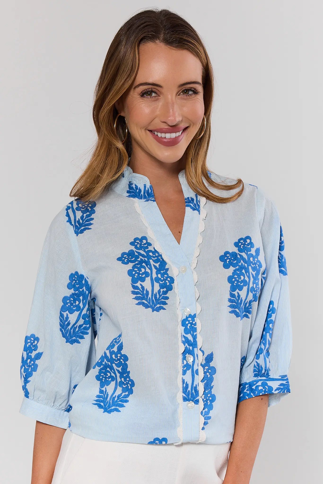 Woman wearing a light blue blouse with blue floral patterns on a white background