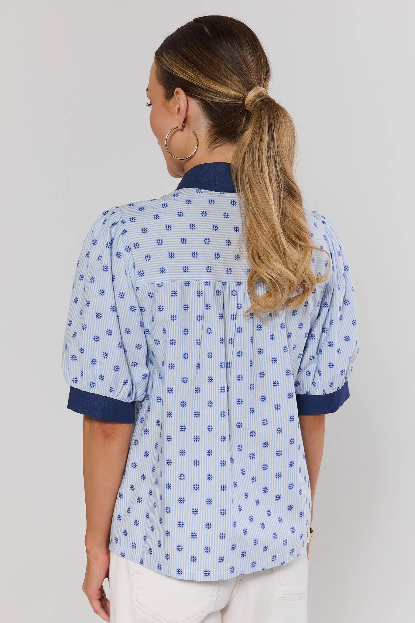 Woman wearing a blue patterned shirt with a plain background standing