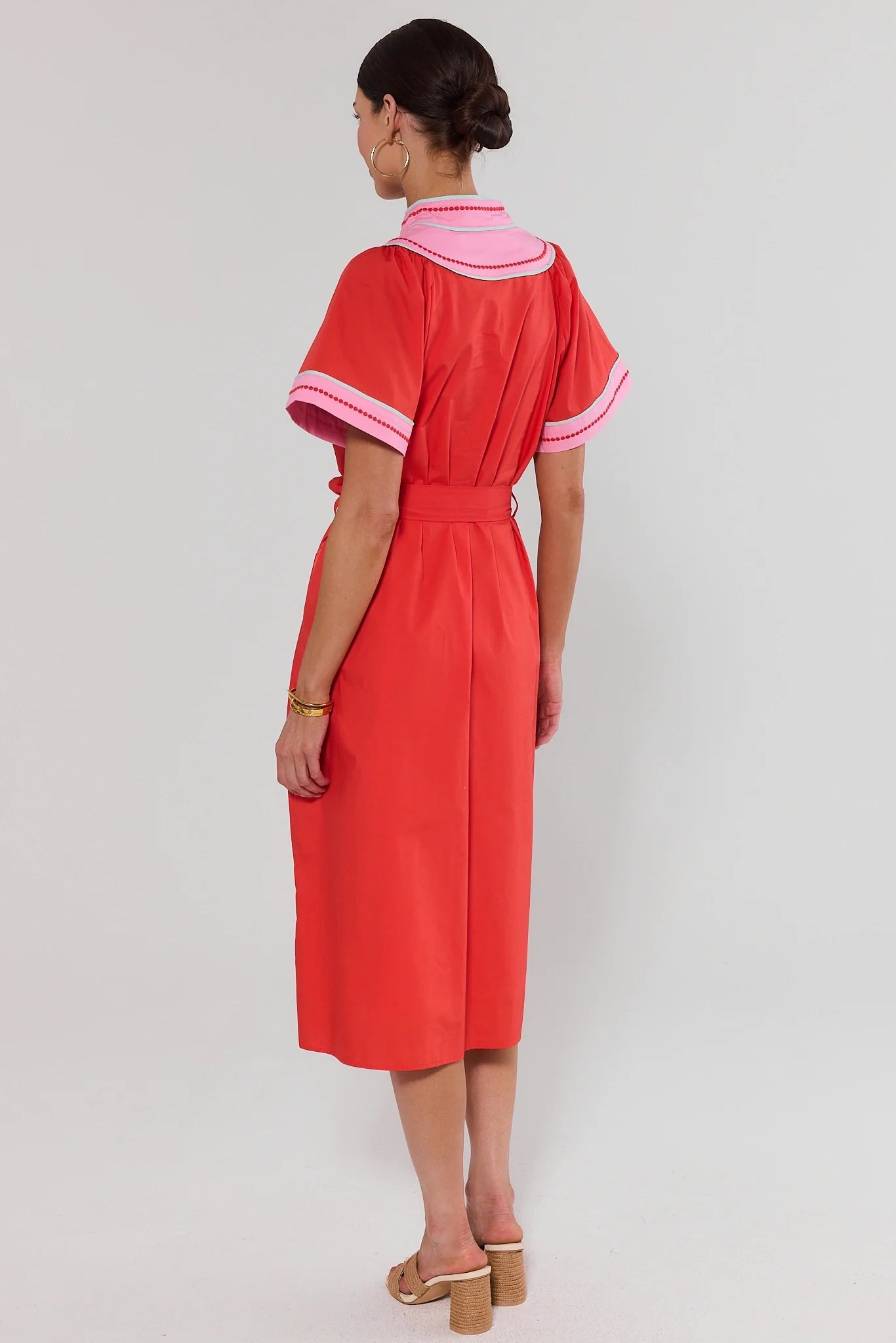 Woman standing wearing a red dress with pink accents on a white background