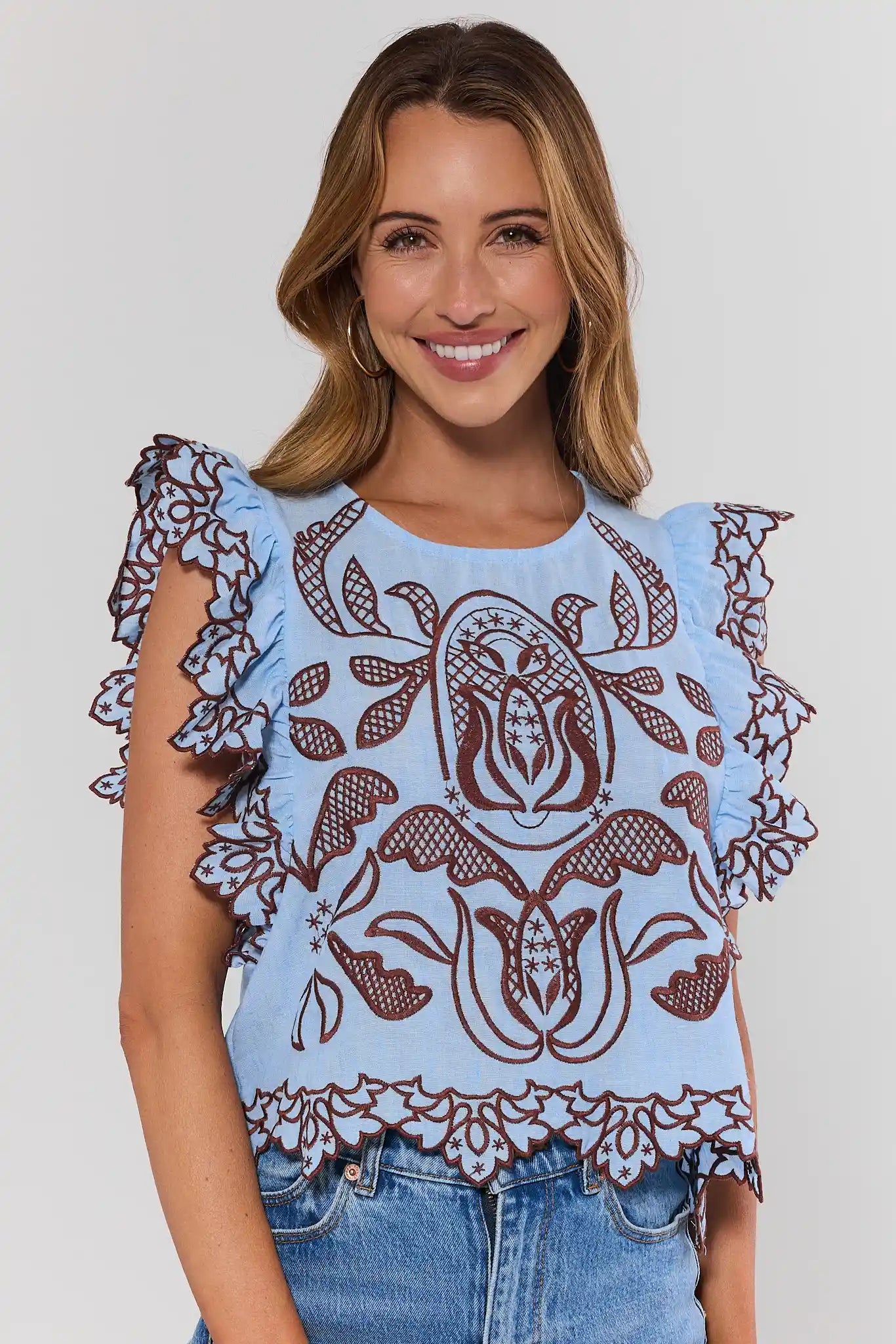 Woman wearing a light blue top with brown lace details on a plain background