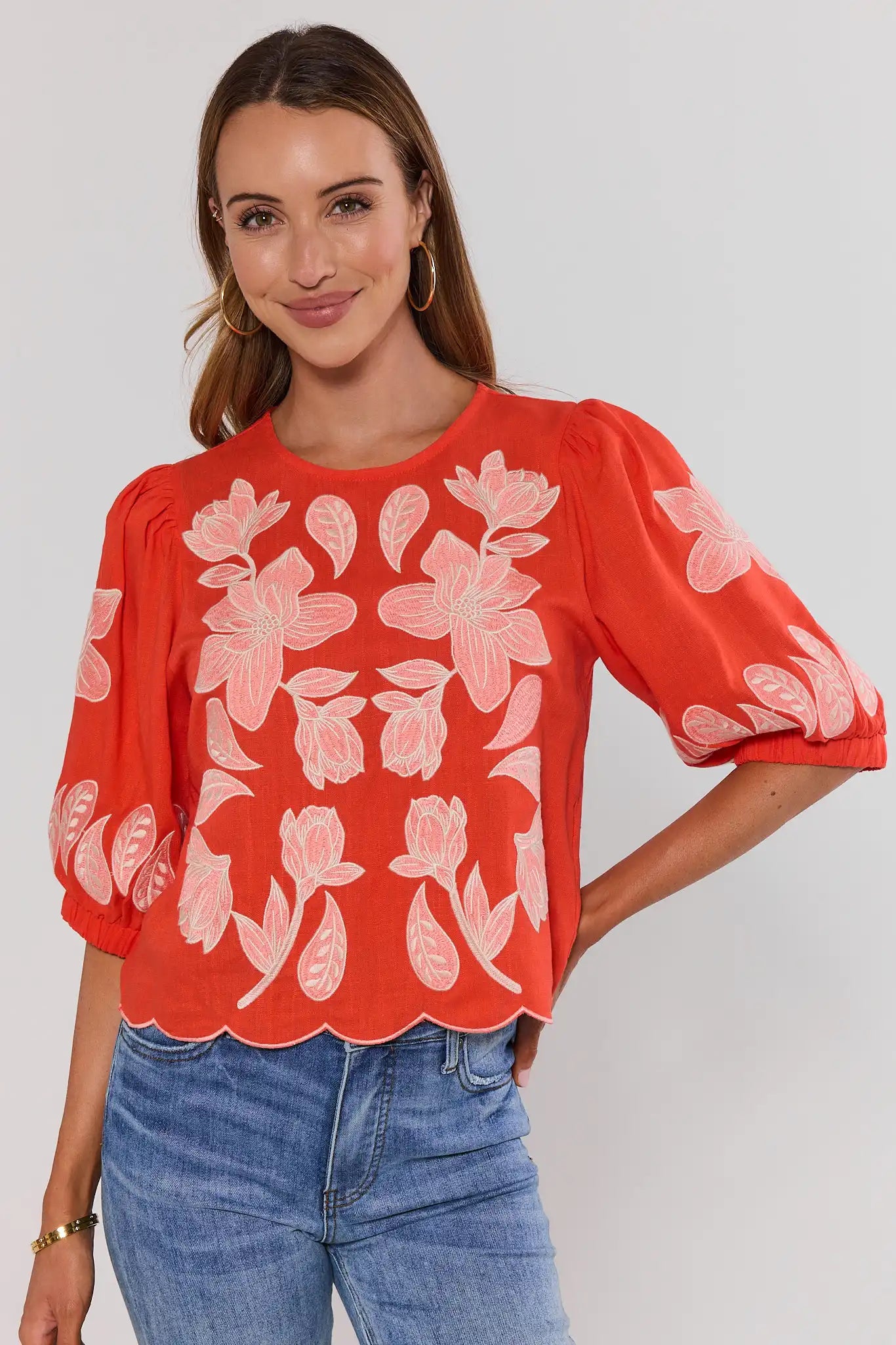 Woman wearing a red floral blouse with blue jeans on a plain background