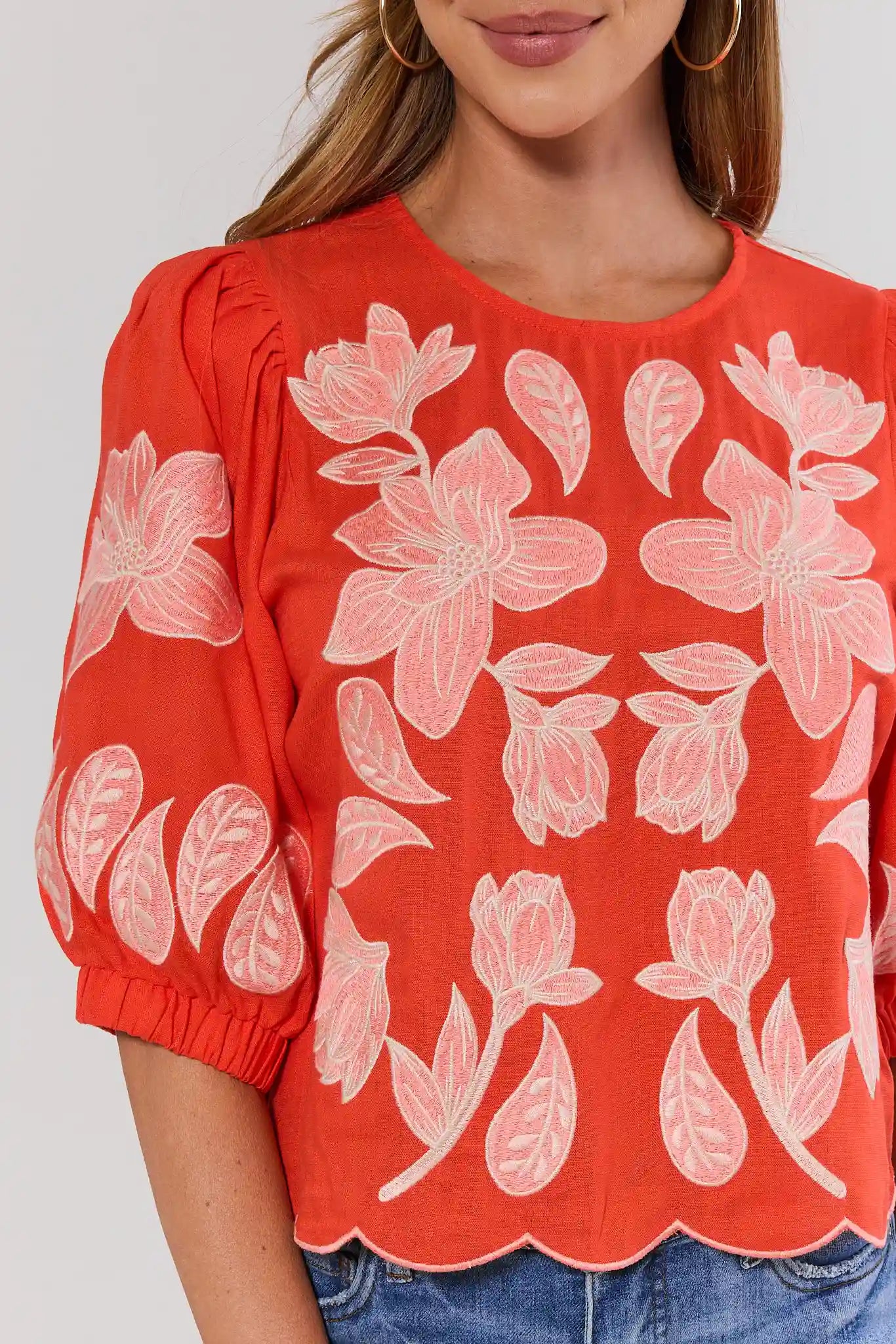 close up orange blouse with white floral pattern worn by a person on a plain background