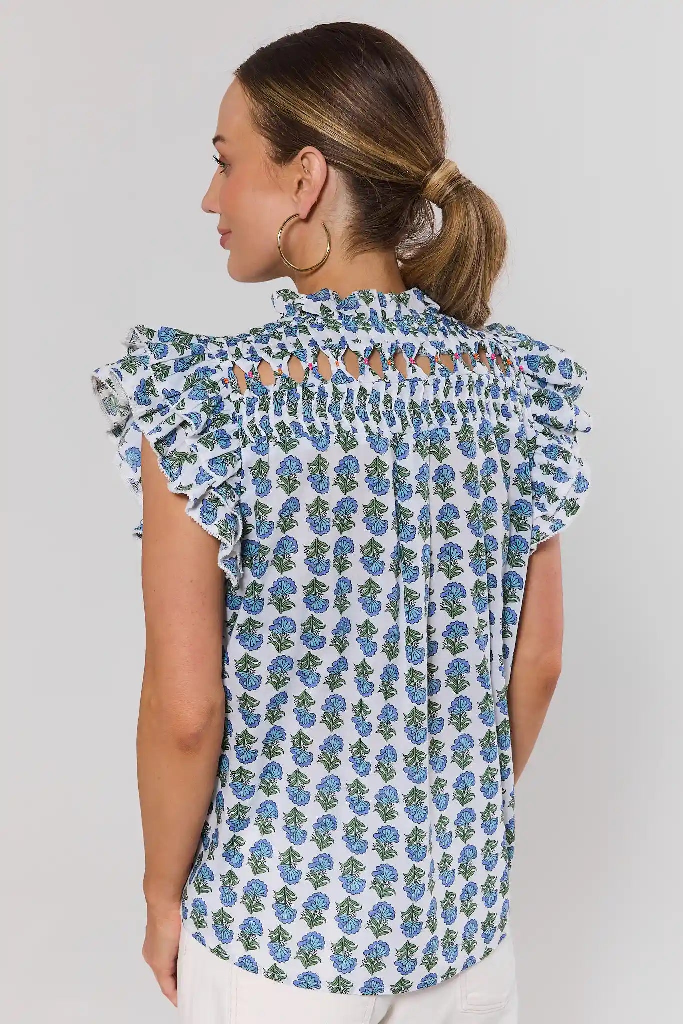 Woman standing wearing a floral blouse with ruffled sleeves on a plain background