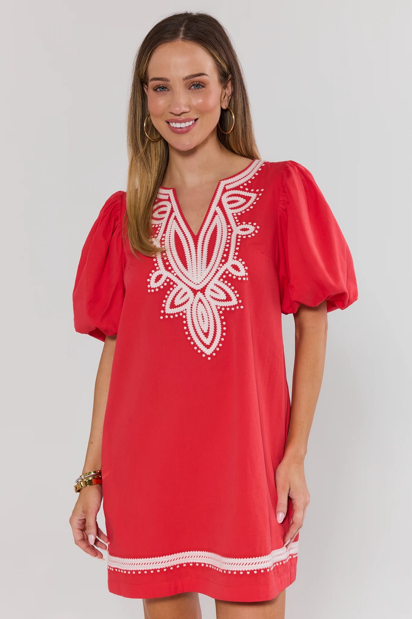 Woman wearing a red dress with white embroidery on a plain background