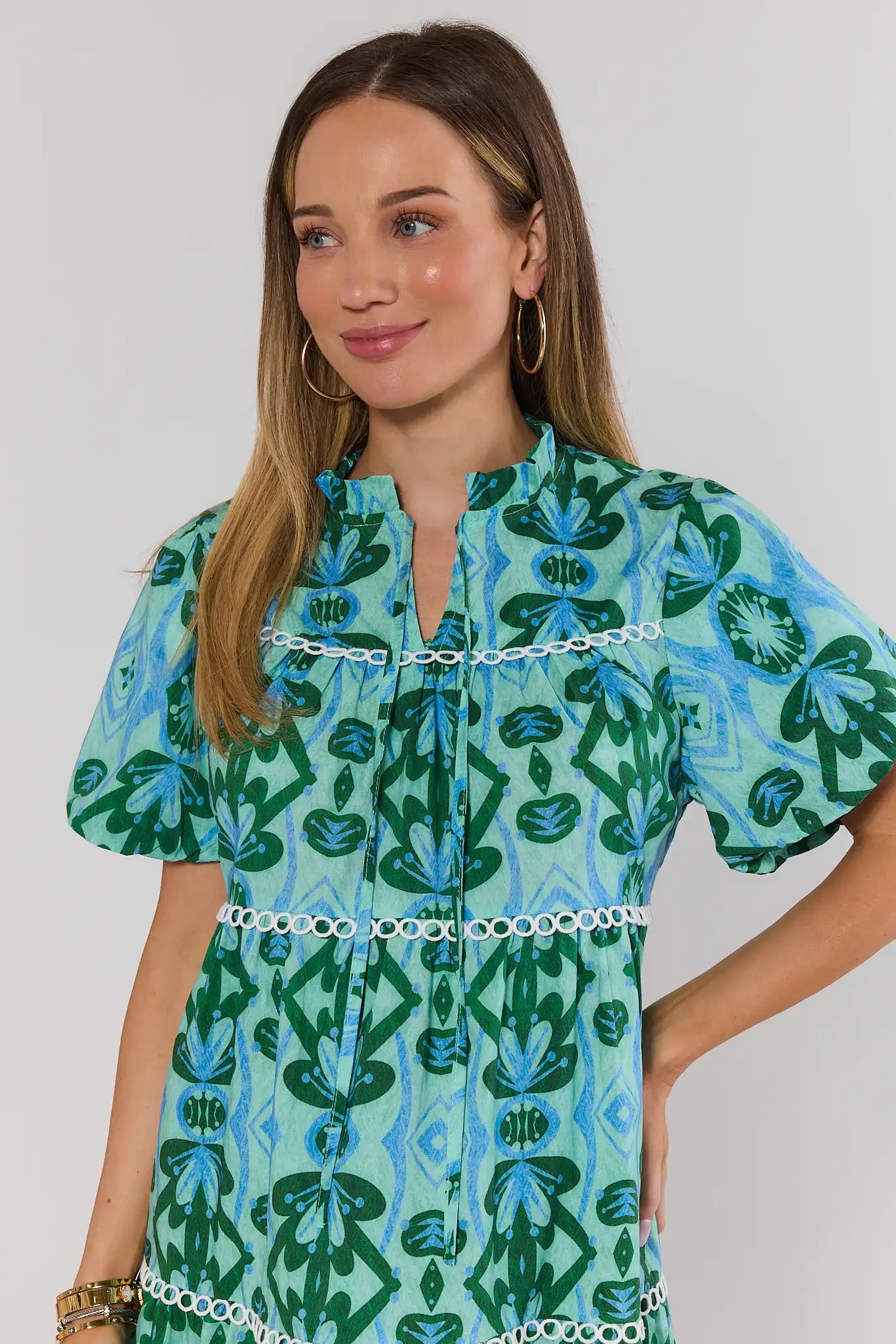 Woman wearing a green and blue patterned dress with a plain background. close up