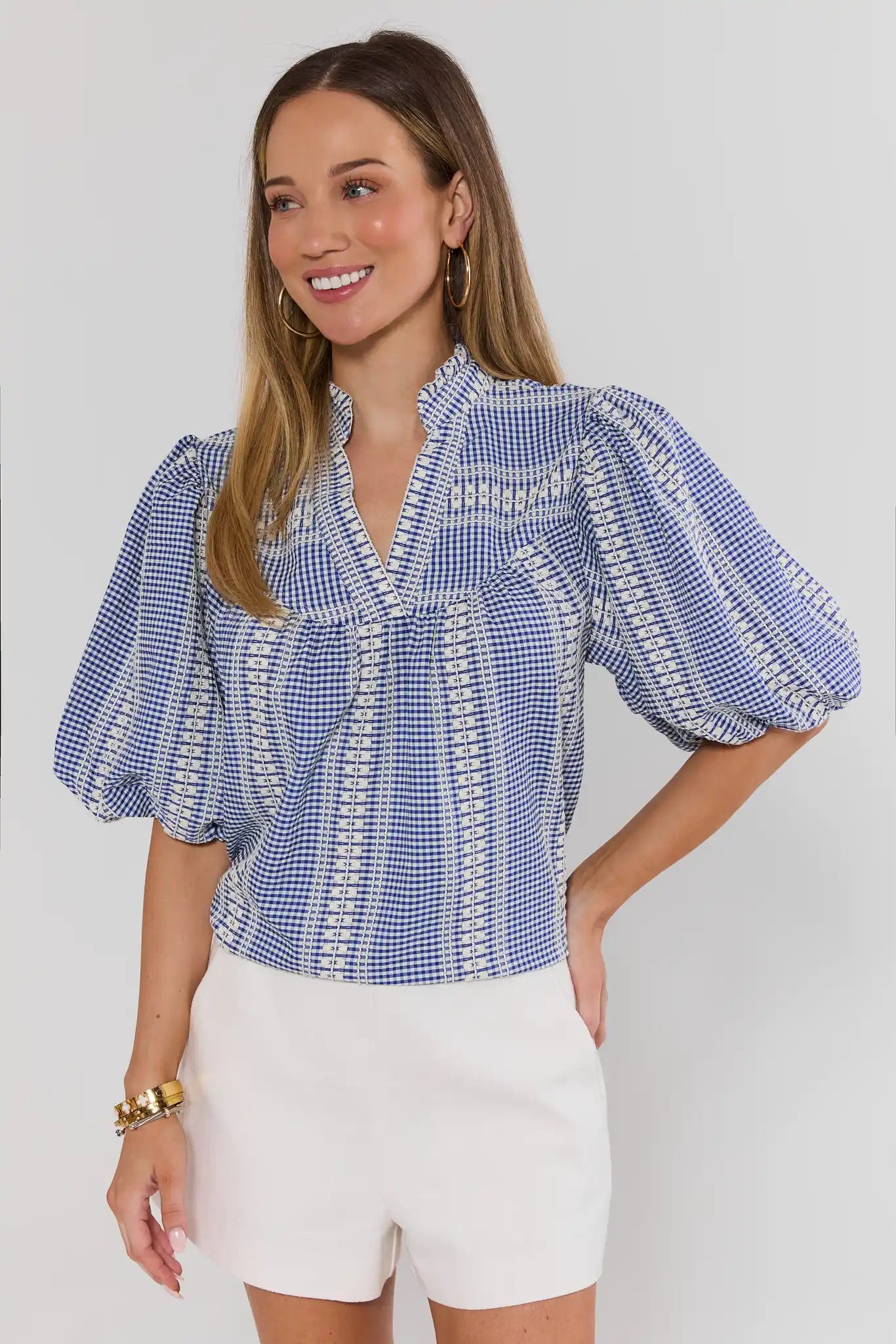 Woman wearing a blue checkered blouse and white shorts on a plain background