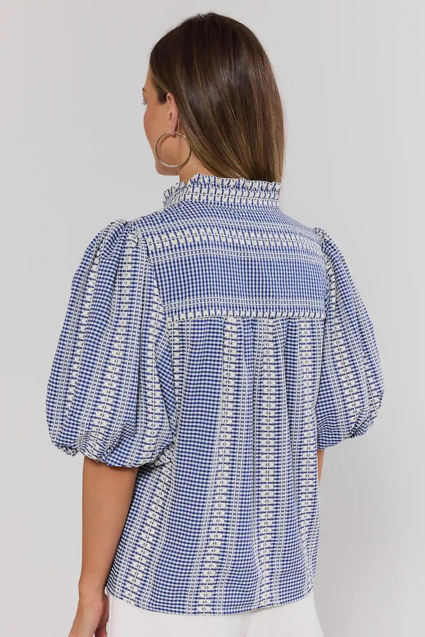 Woman wearing a blue and white checkered blouse with puff sleeves on a plain background standing