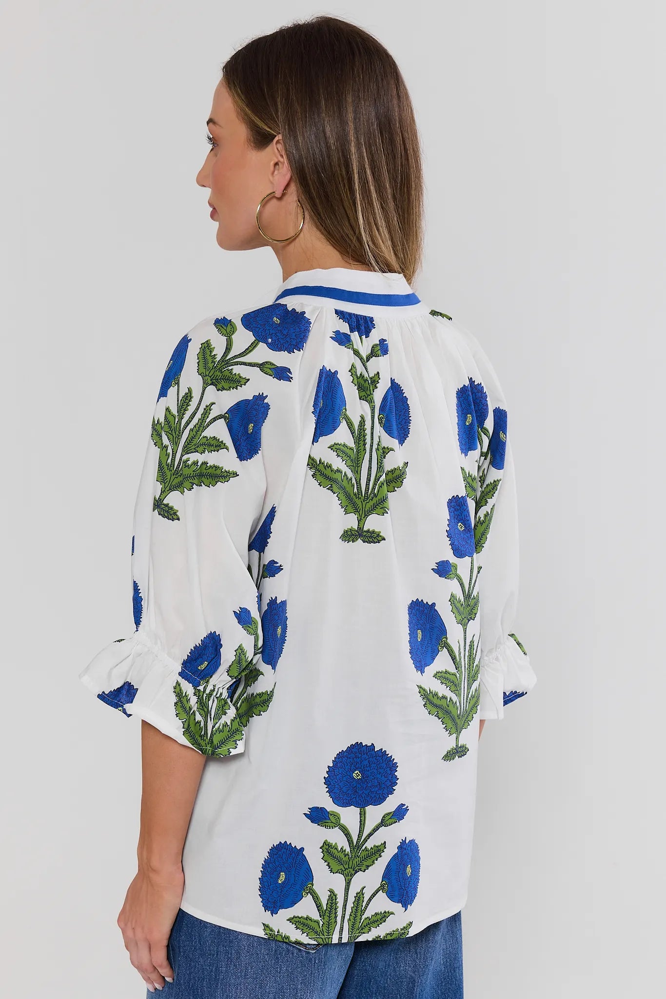 Woman standing wearing a white blouse with blue floral embroidery on a plain background