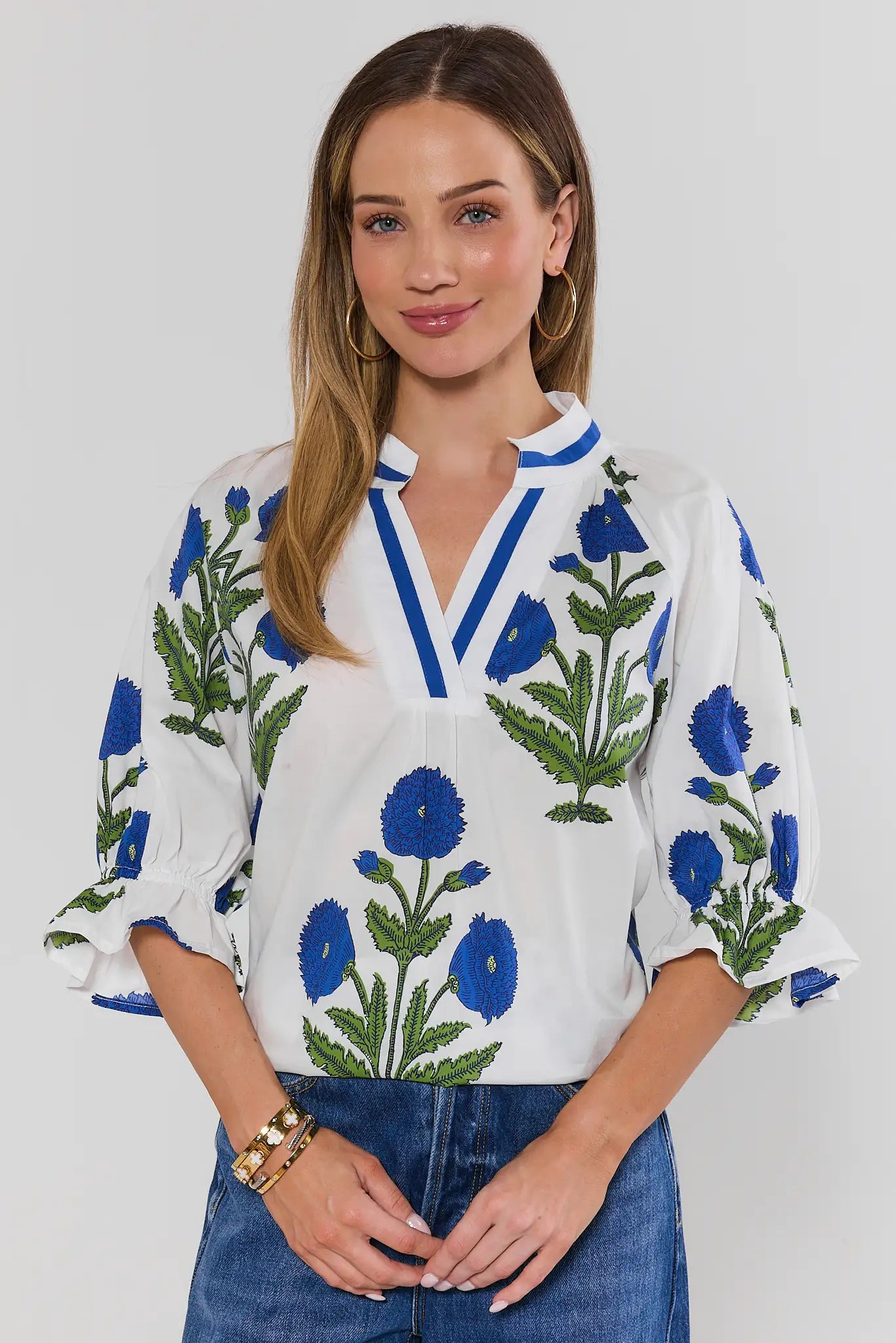 Woman wearing a white blouse with blue floral embroidery on a plain background