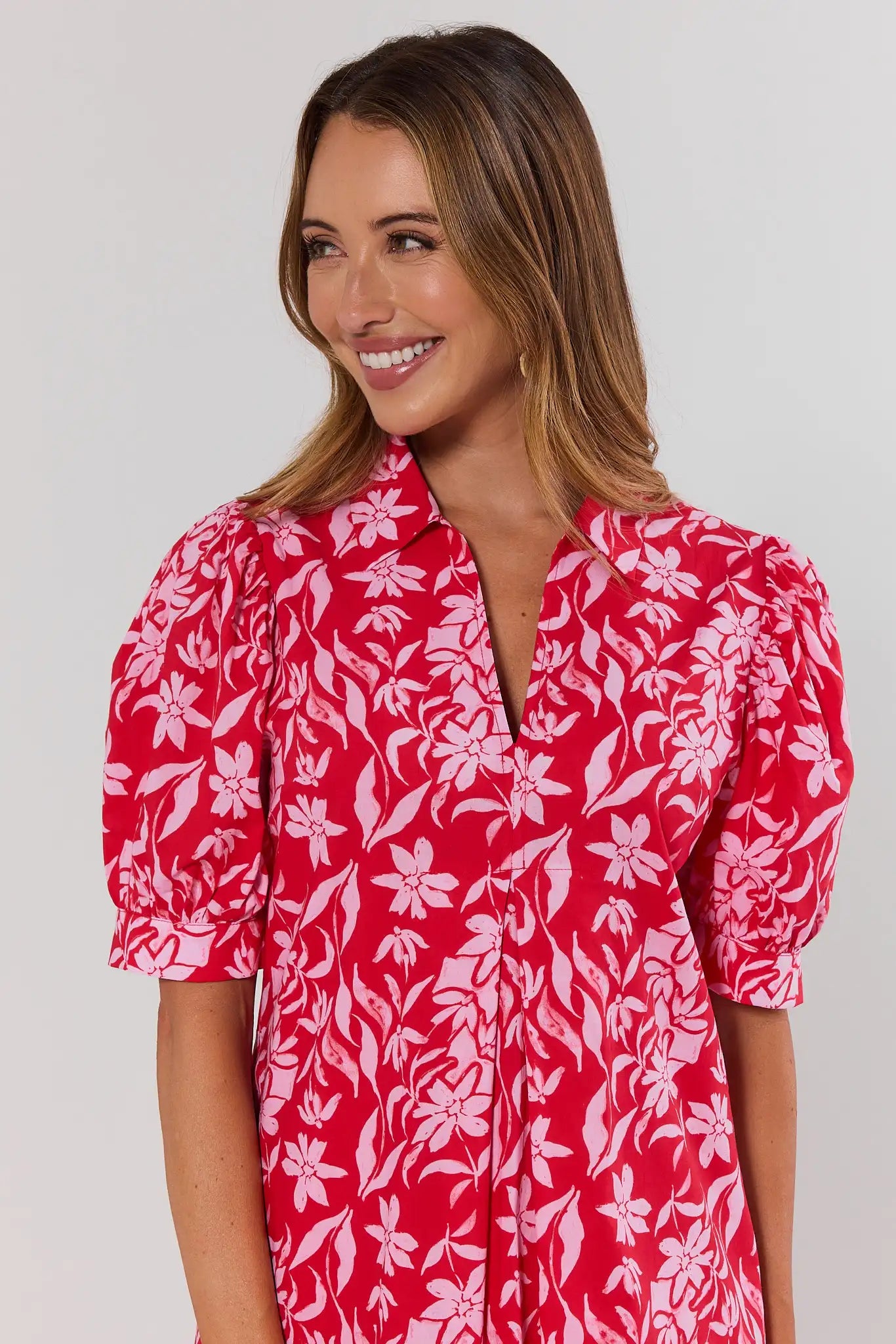 Woman wearing a red floral dress against a plain background close up