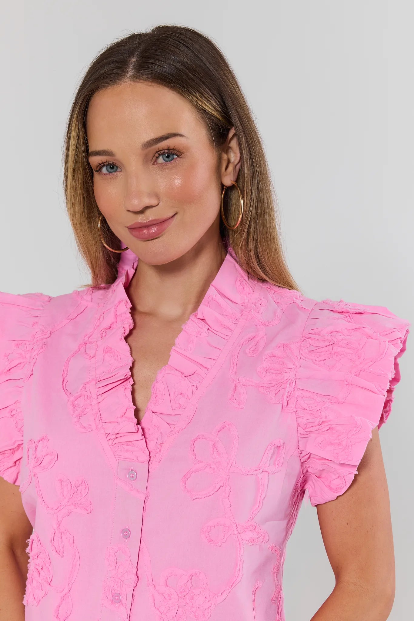 close up Woman wearing a pink blouse with ruffled sleeves against a plain background