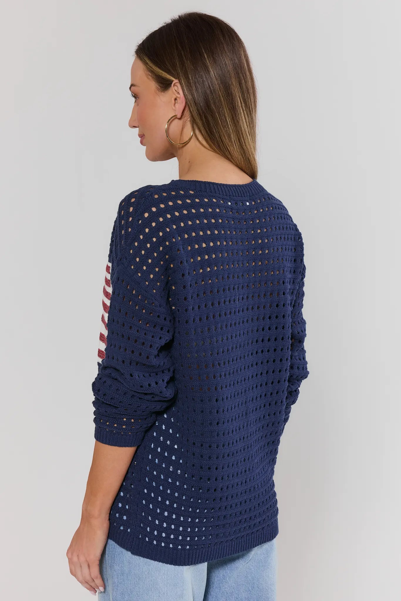 Woman standing wearing a navy blue crochet sweater with a pattern on a plain background