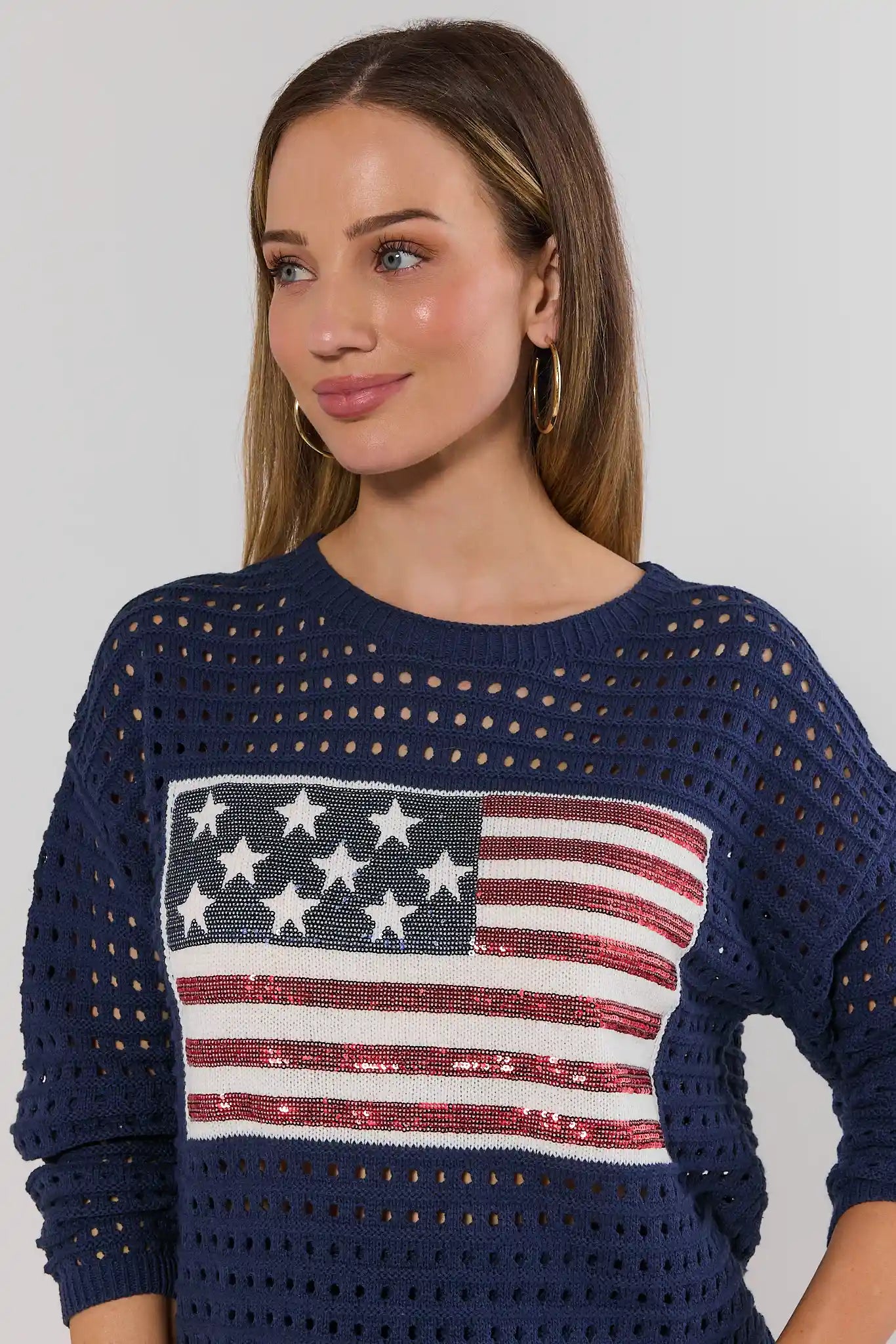close up Woman wearing a navy blue sweater with an American flag design on a plain background