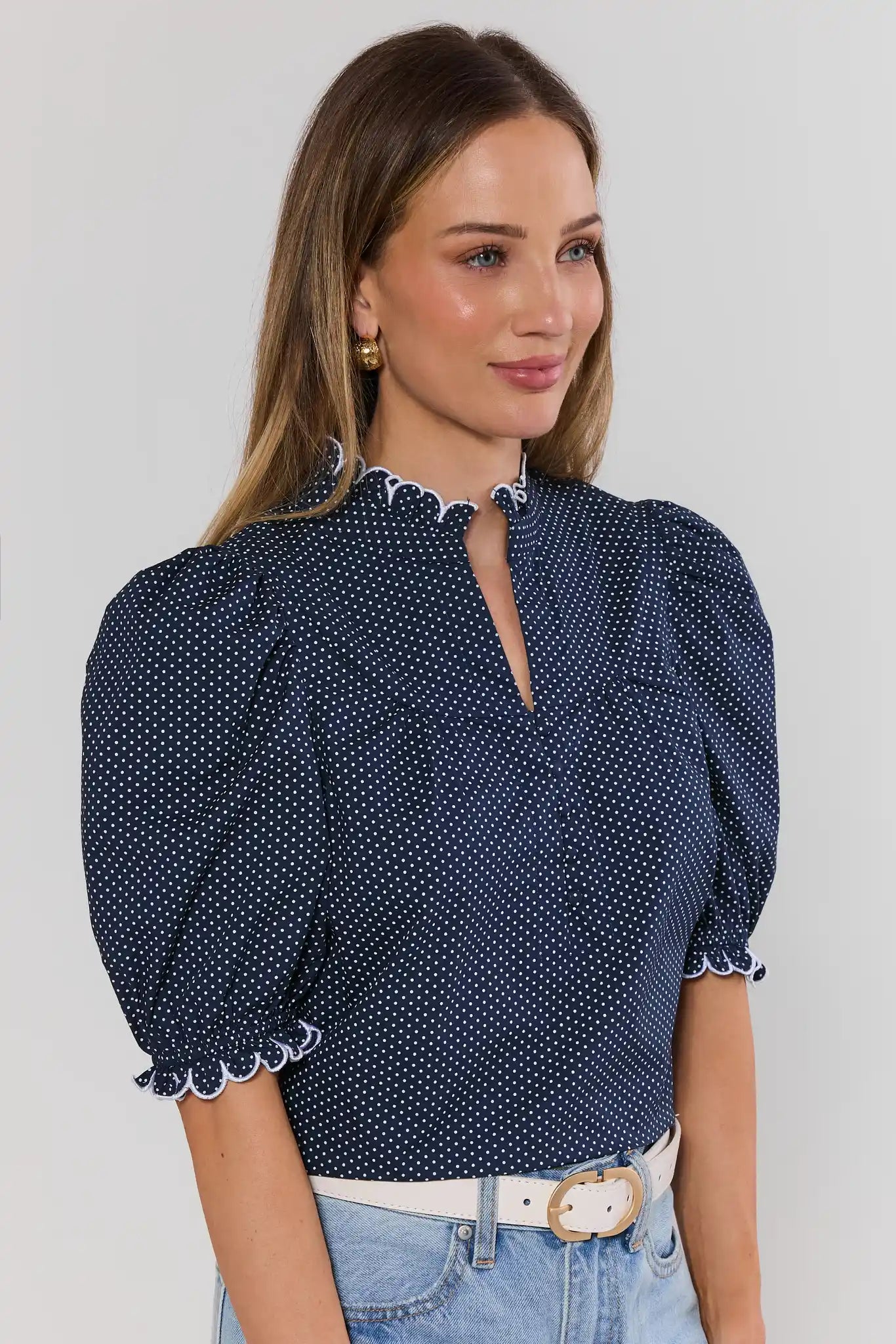 Woman wearing a navy blue polka dot blouse with puffed sleeves against a light gray background side