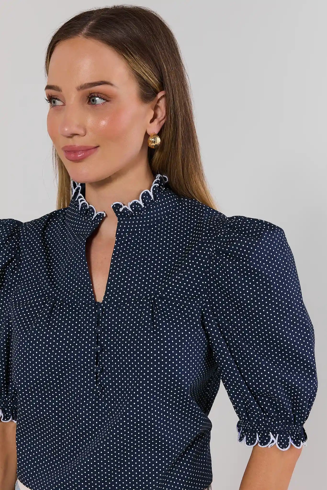 Woman wearing a navy blue polka dot blouse with white trim on a gray background close up