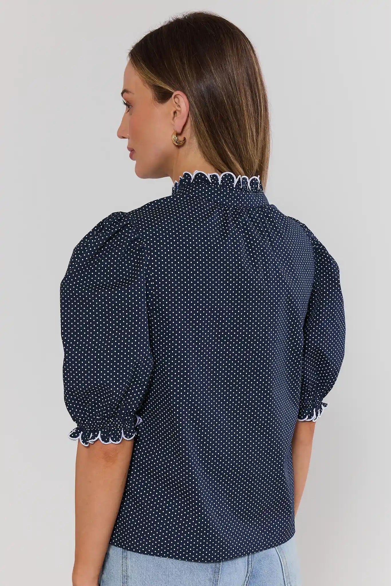 Woman stand wearing a navy blue blouse with white polka dots on a light gray background