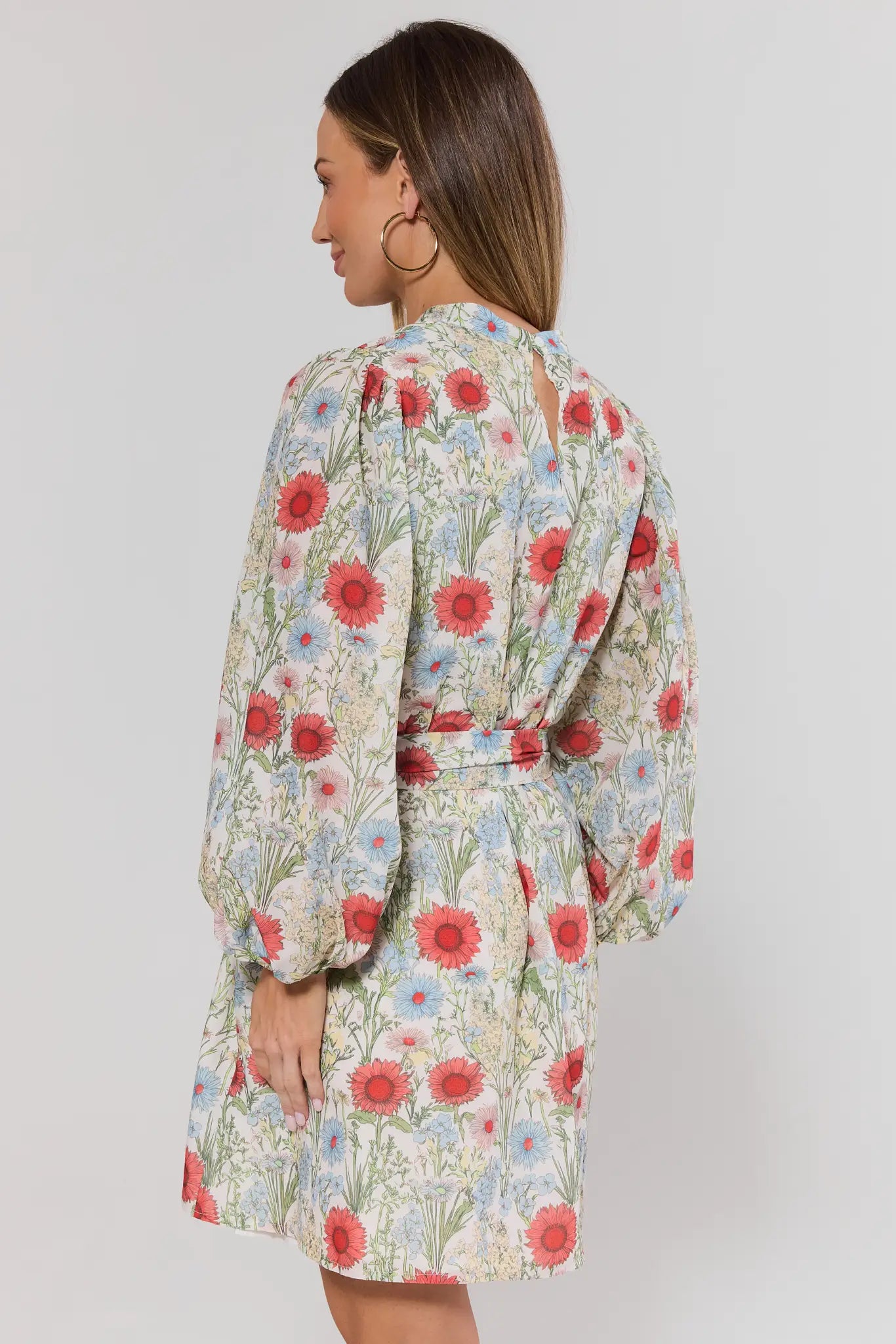 Woman standing wearing a floral dress with a plain background