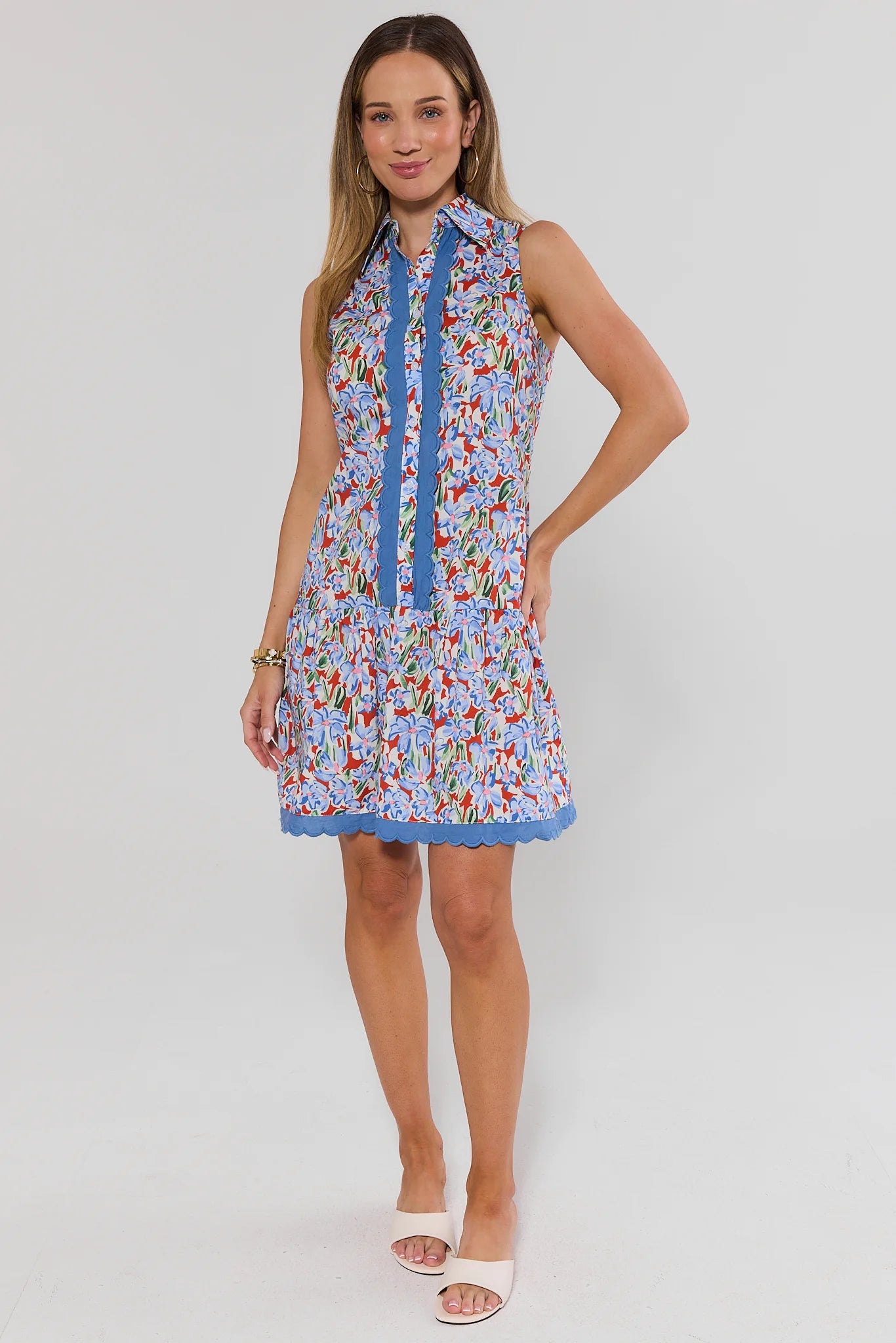 Woman wearing a colorful floral dress with a blue collar on a white background standing