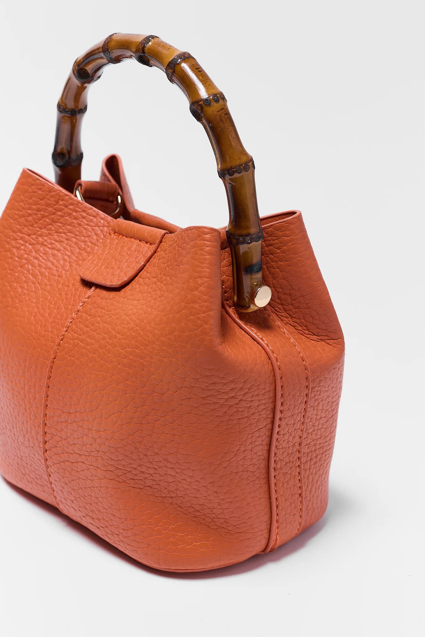 Orange leather handbag with a bamboo handle on a white background close up