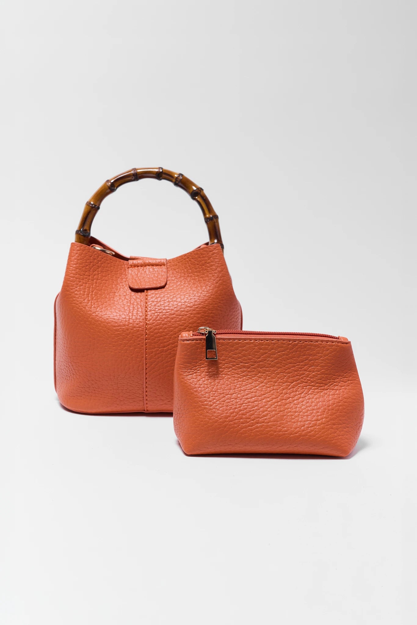 Orange leather handbag with bamboo handle and matching pouch on a light gray background
