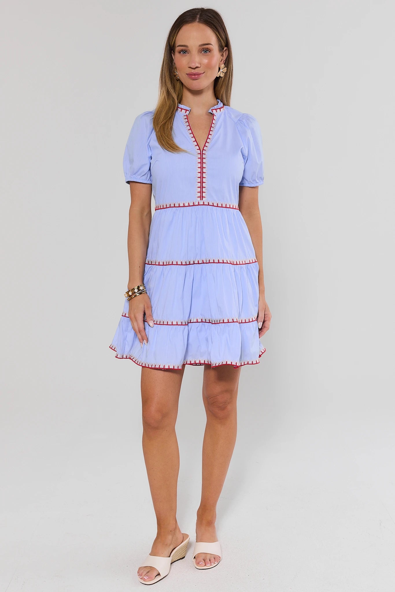 Woman wearing a light blue dress with red trim on a white background stand