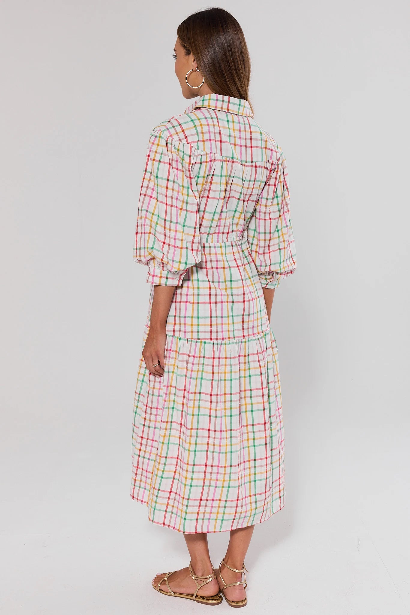 Woman wearing a colorful checkered dress on a white background standing