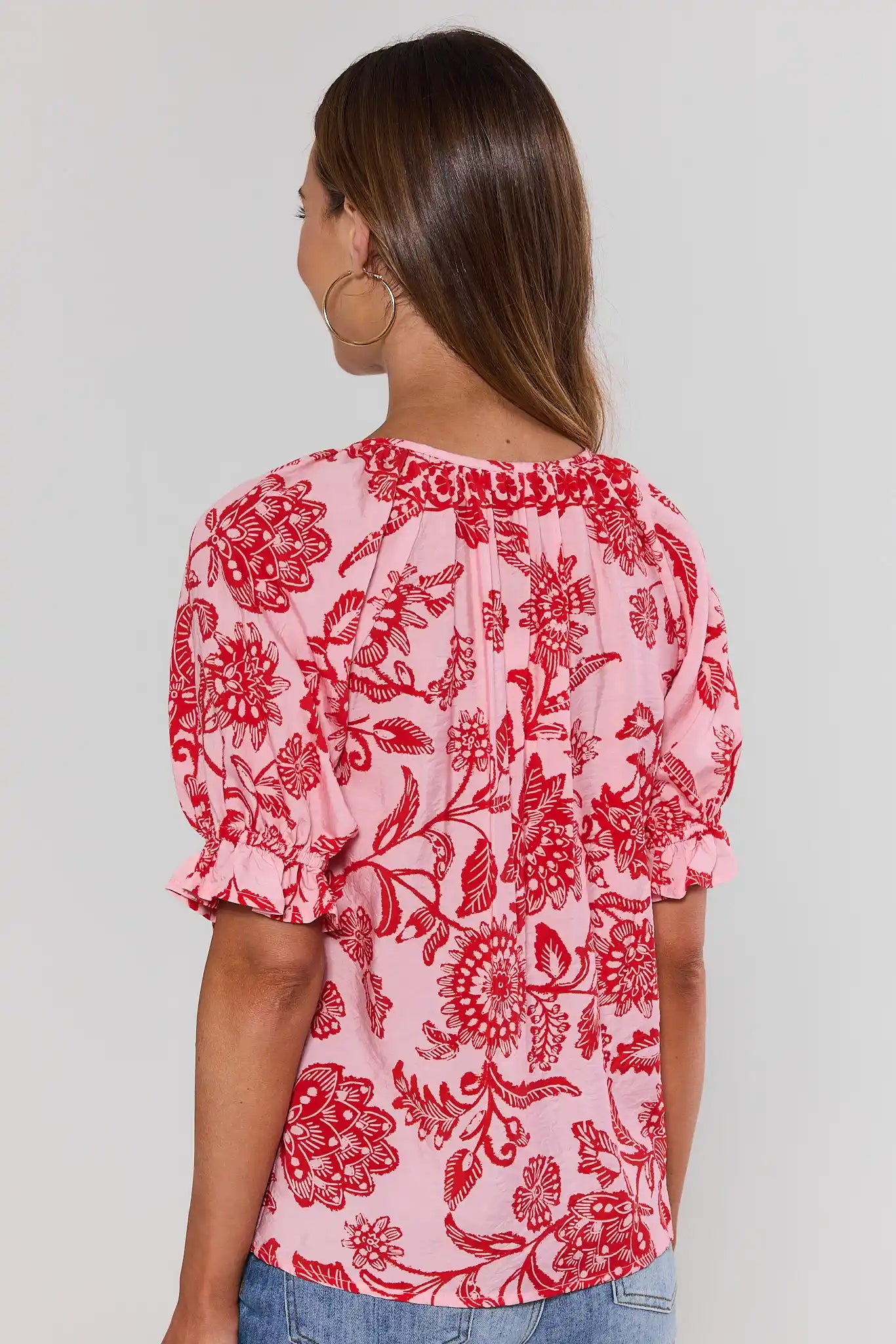 Woman standing wearing a red floral blouse against a plain background