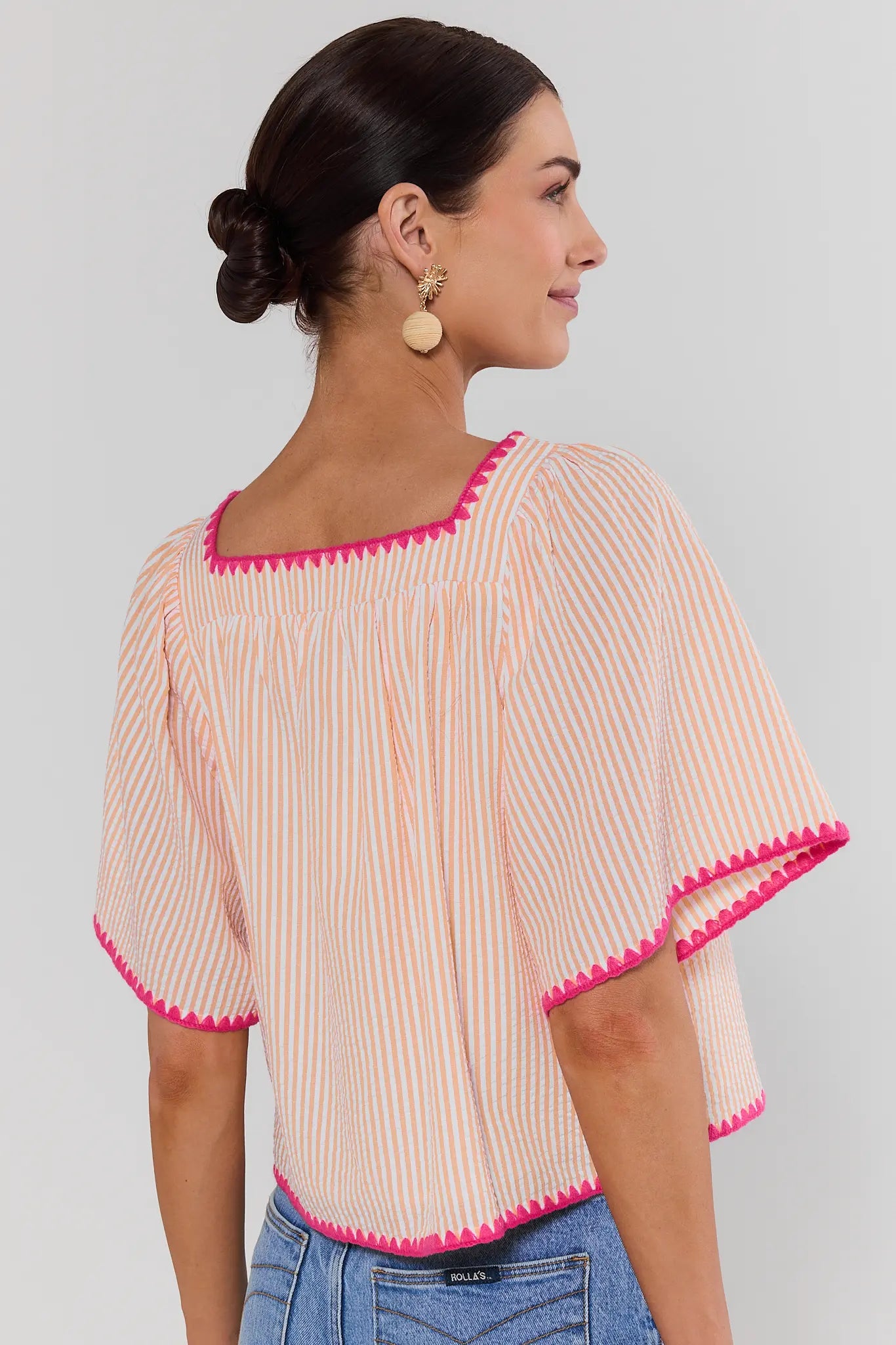 Woman wearing a striped blouse with pink trim on a plain background standing