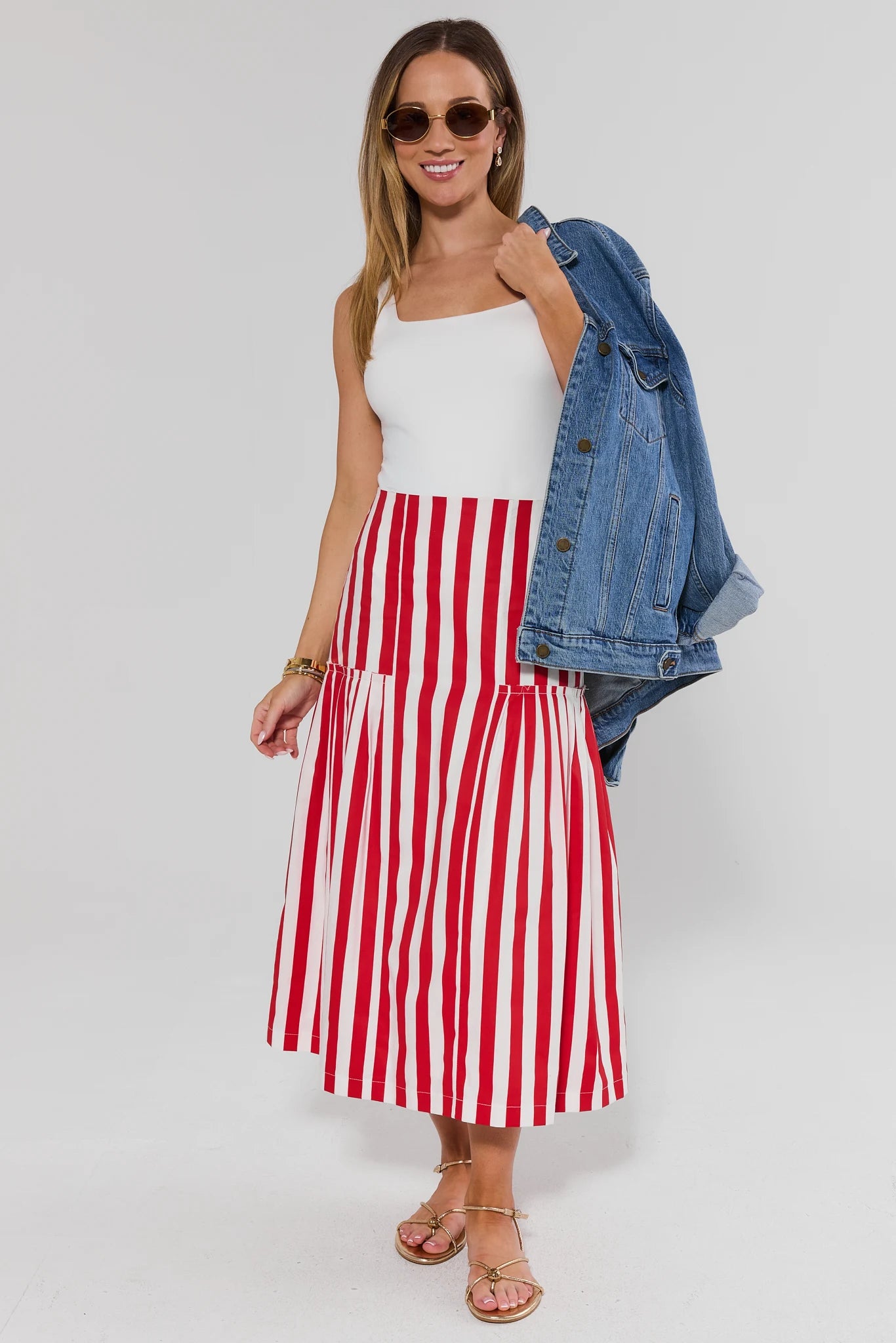 Woman wearing a white top and red and white striped skirt with a denim jacket on a white background