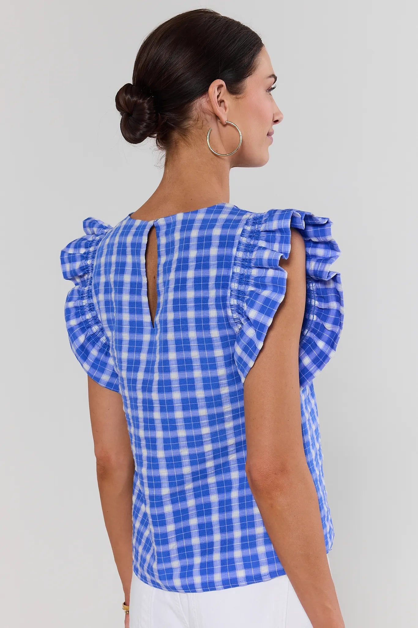 Woman wearing a blue and white checkered top standing with ruffled sleeves on a plain background 