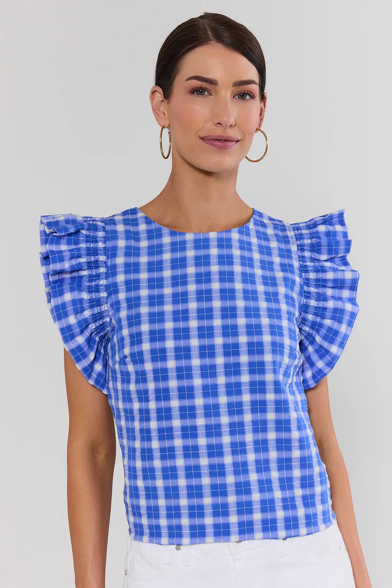 Woman wearing a blue and white checkered top with ruffled sleeves on a plain background