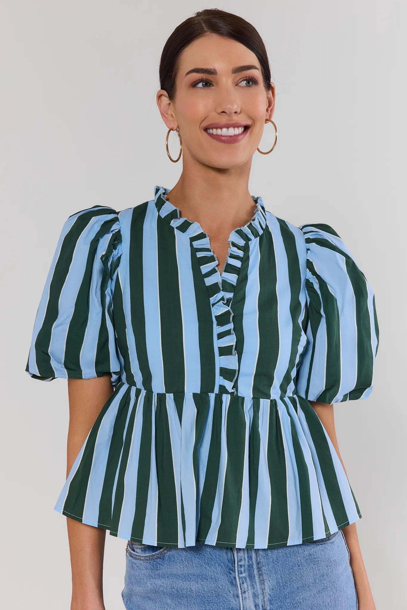 Woman wearing a green and blue striped peplum top against a plain background
