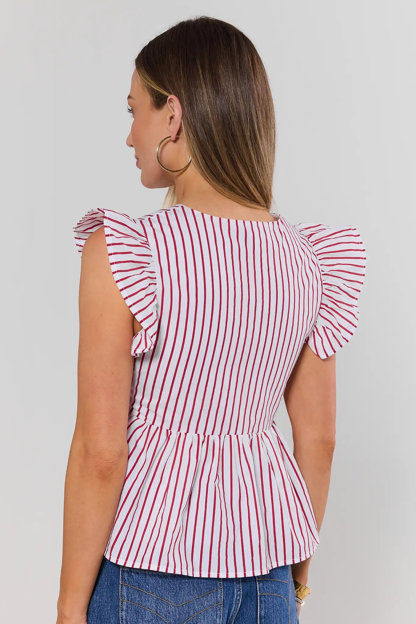 Woman wearing a red and white striped top with ruffled sleeves on a plain background standing