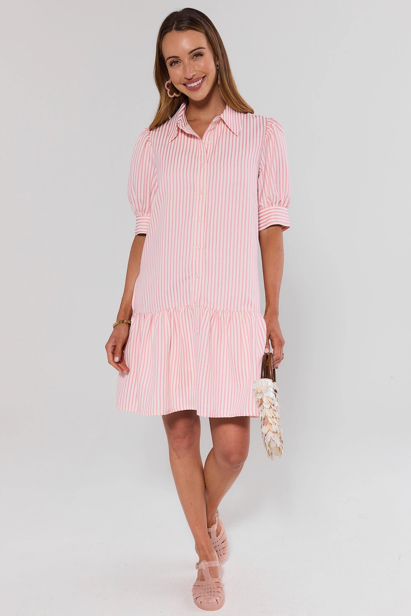 Woman standing wearing a pink and white striped dress on a plain background