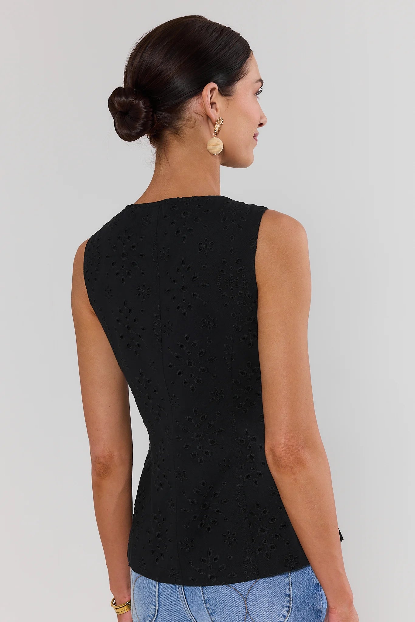Woman wearing a black sleeveless top with a textured pattern on a plain background standing