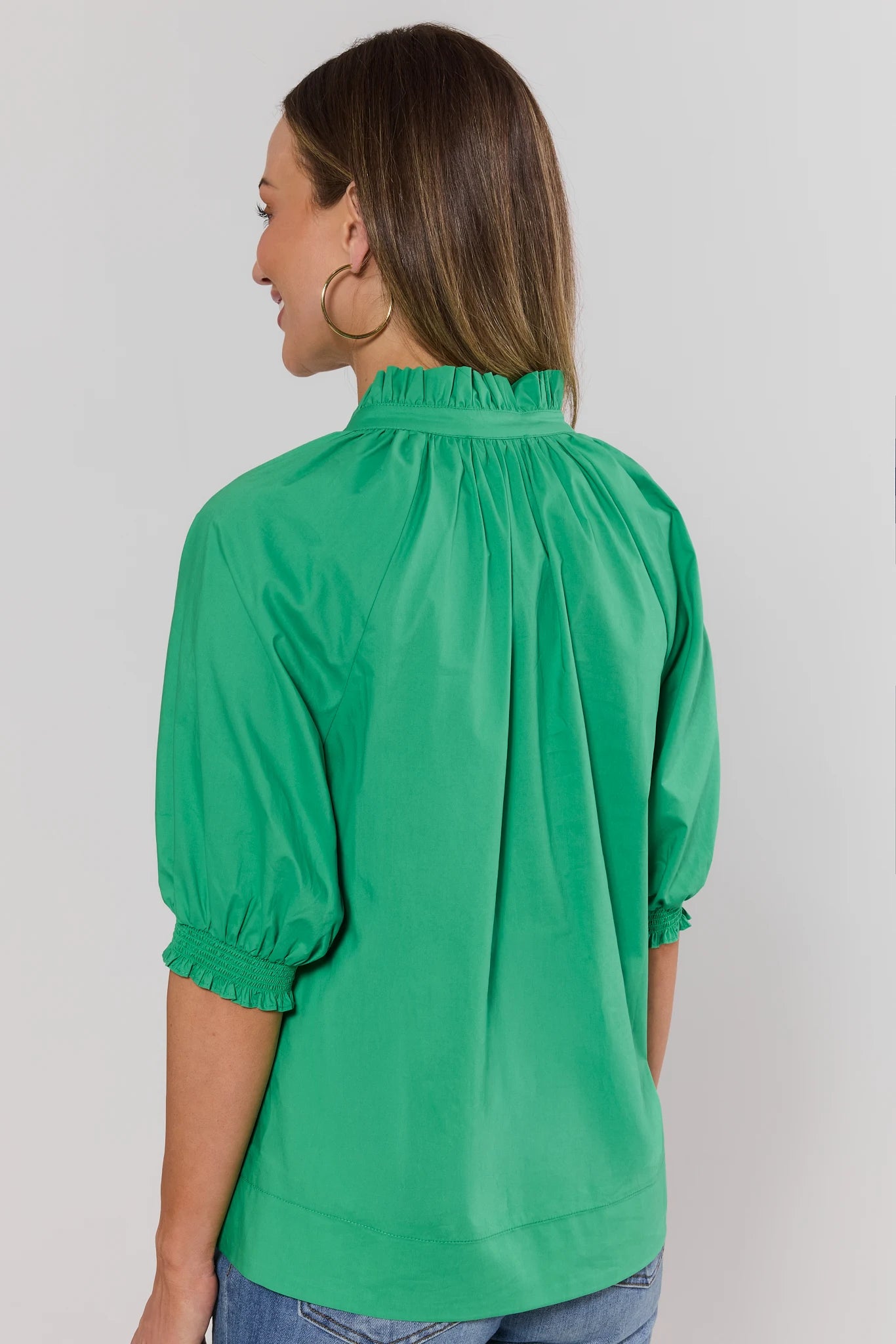 Woman standing wearing a green blouse against a plain background