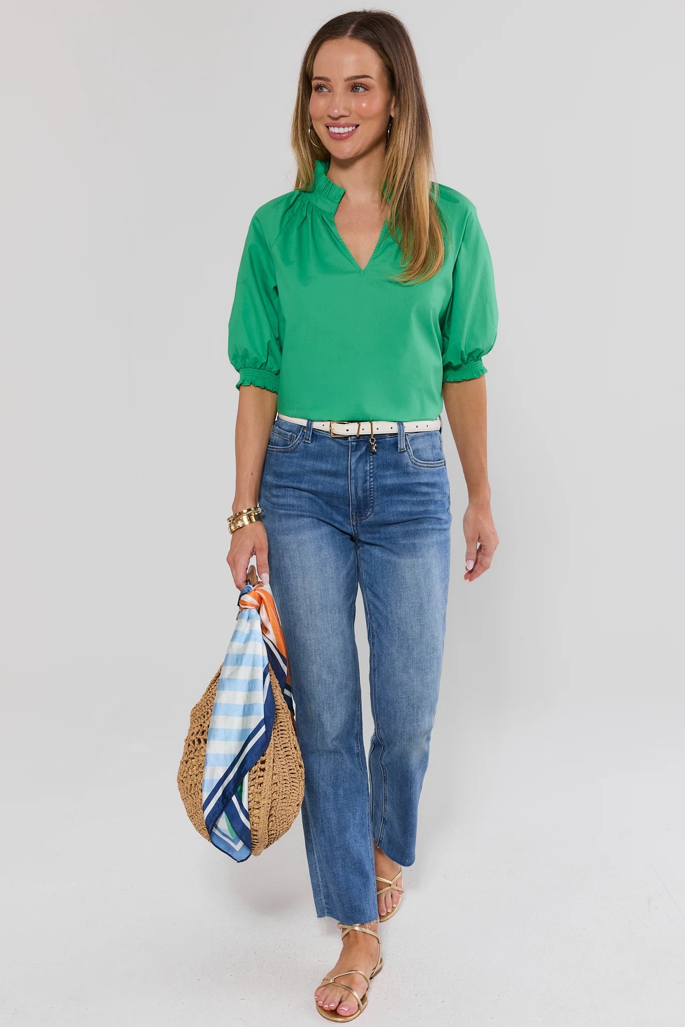 Woman wearing a green blouse and blue jeans, holding a striped bag on a white background
