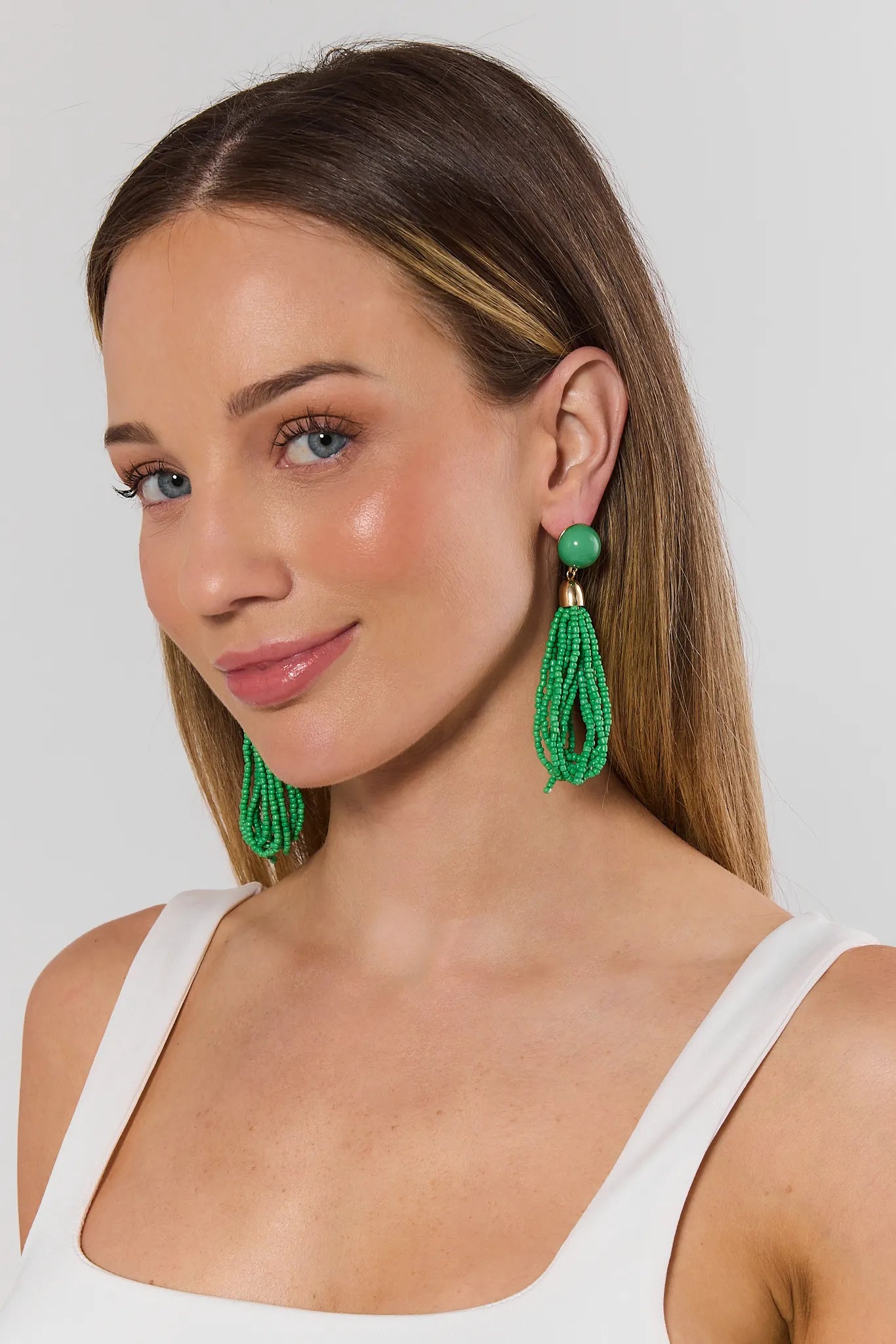 Woman wearing green beaded earrings against a plain background