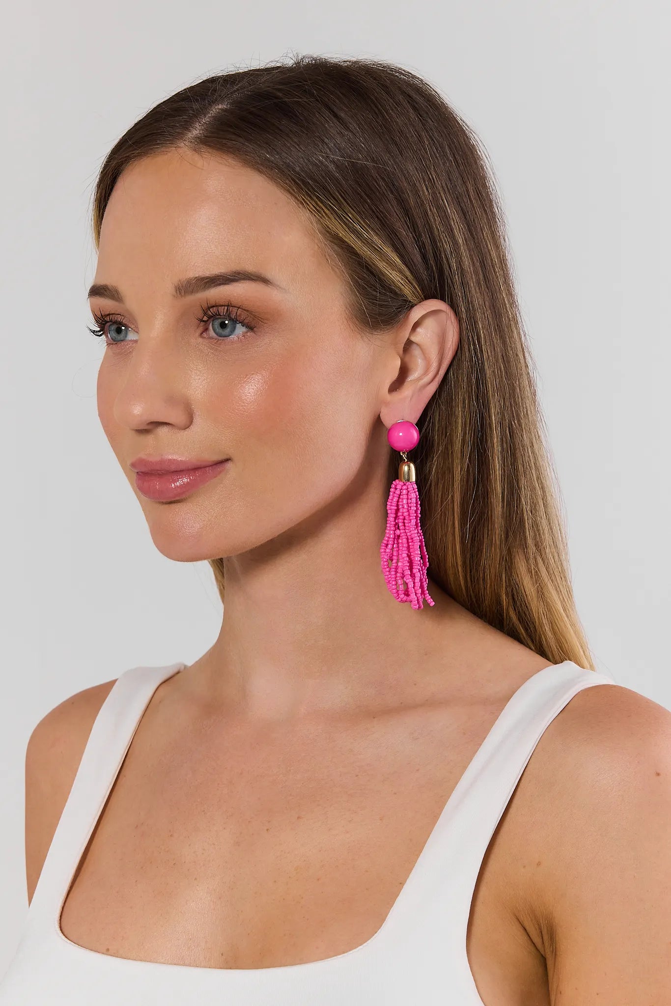 Woman wearing pink tassel earrings against a plain background