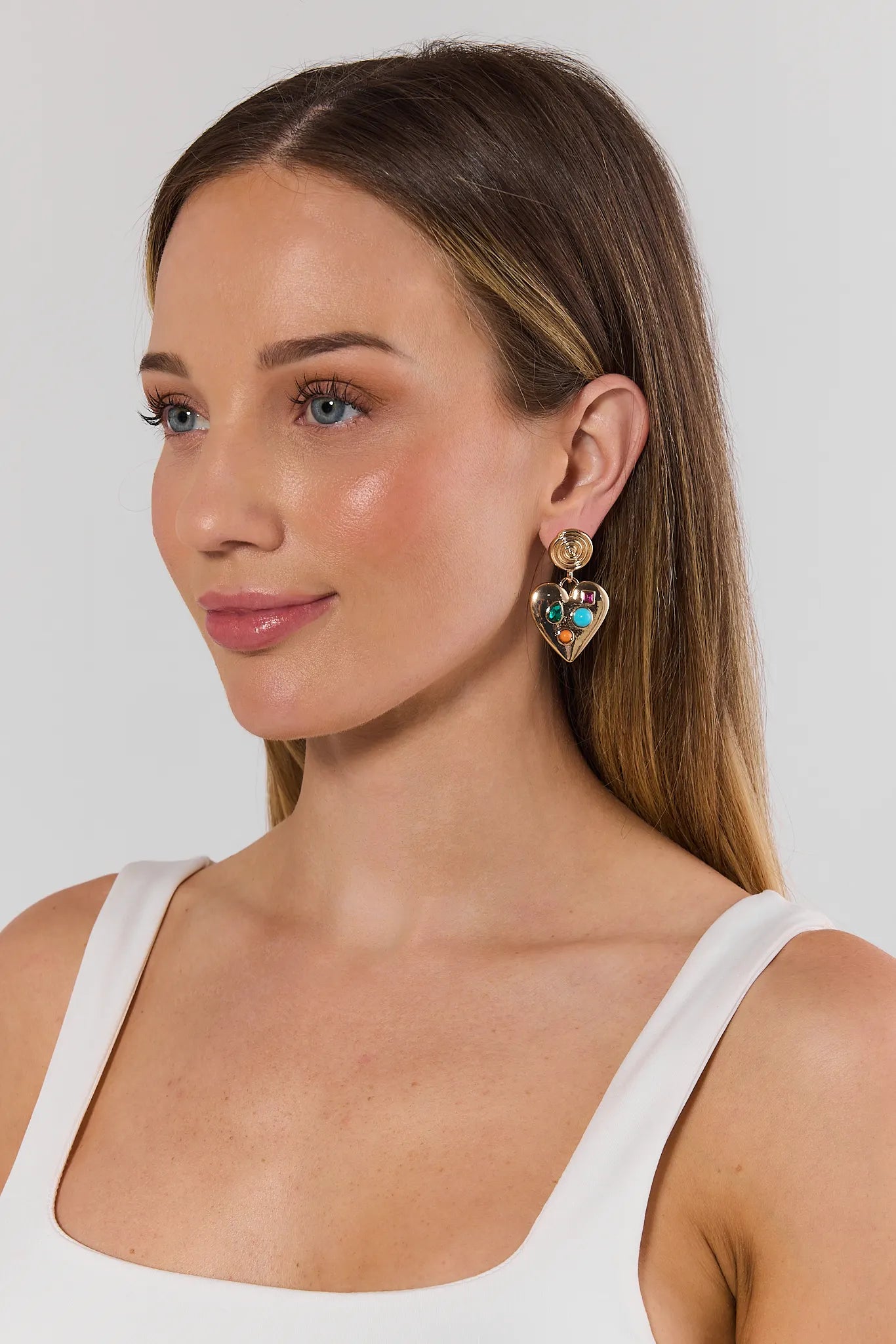 Woman wearing gold earrings with green gemstones against a plain background