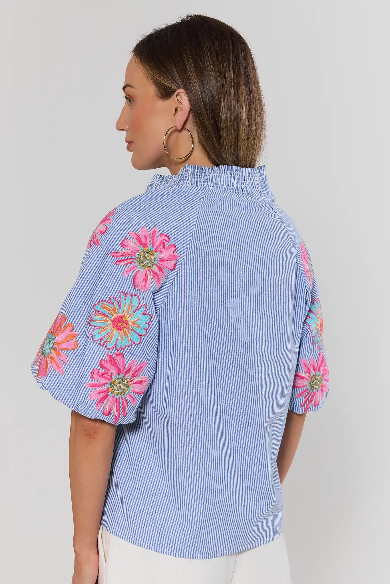 Woman standing wearing a blue striped blouse with colorful floral patterns on a plain background