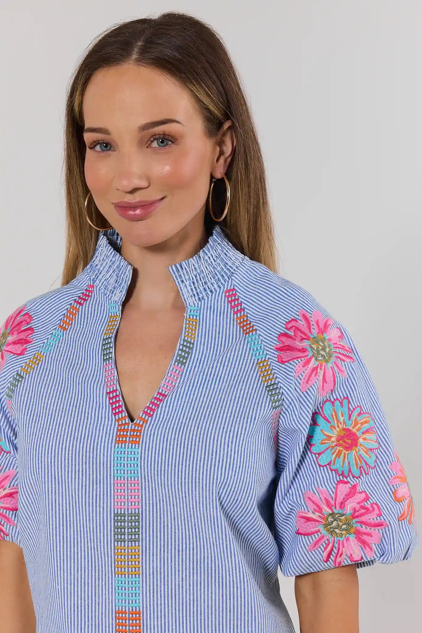 Woman close up wearing a blue and pink embroidered blouse against a white background
