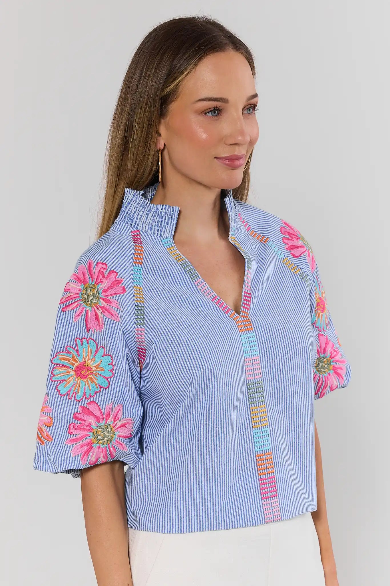 side Woman wearing a blue and white striped blouse with colorful floral embroidery on a plain background