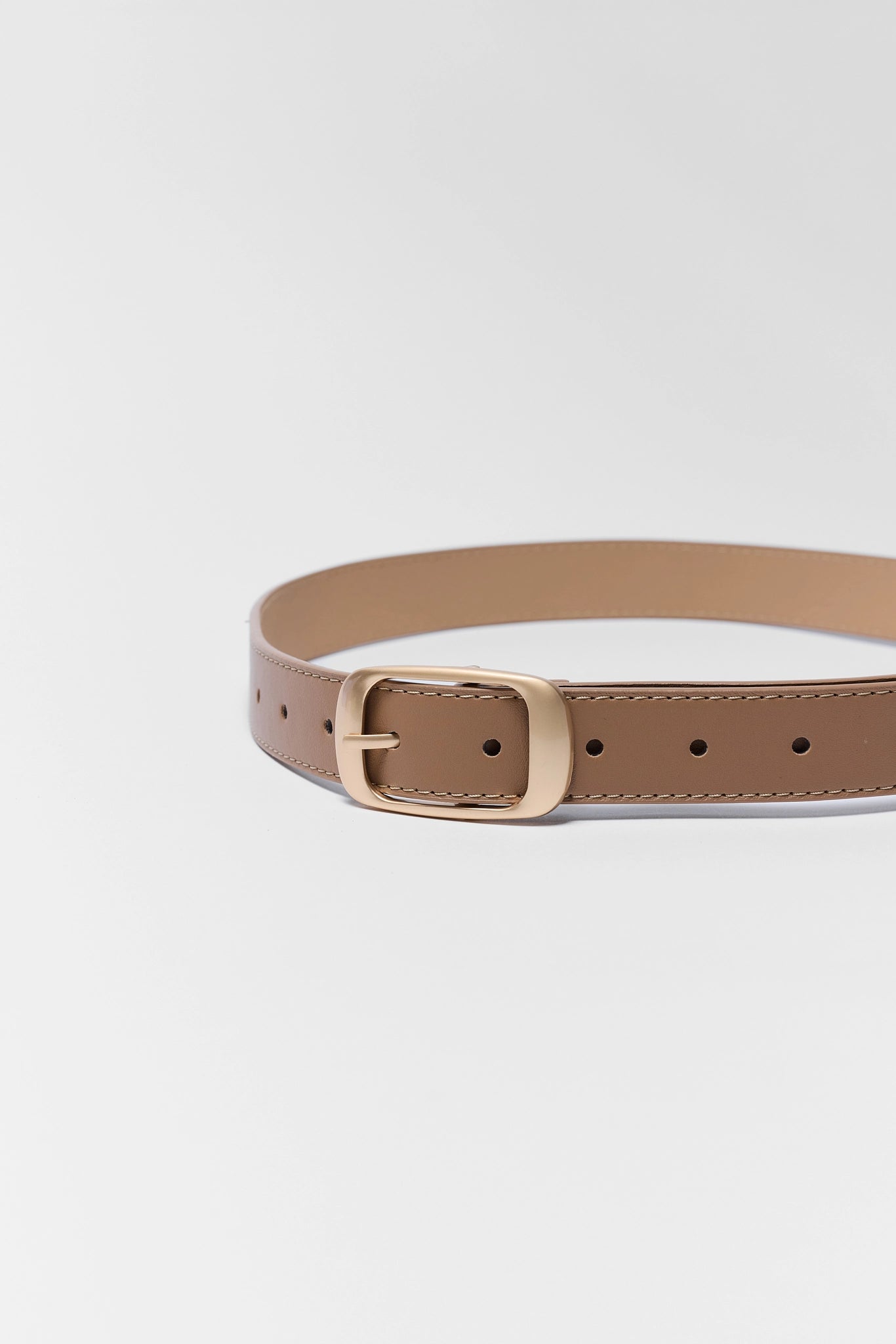 Tan belt with a gold buckle on a light gray background close up