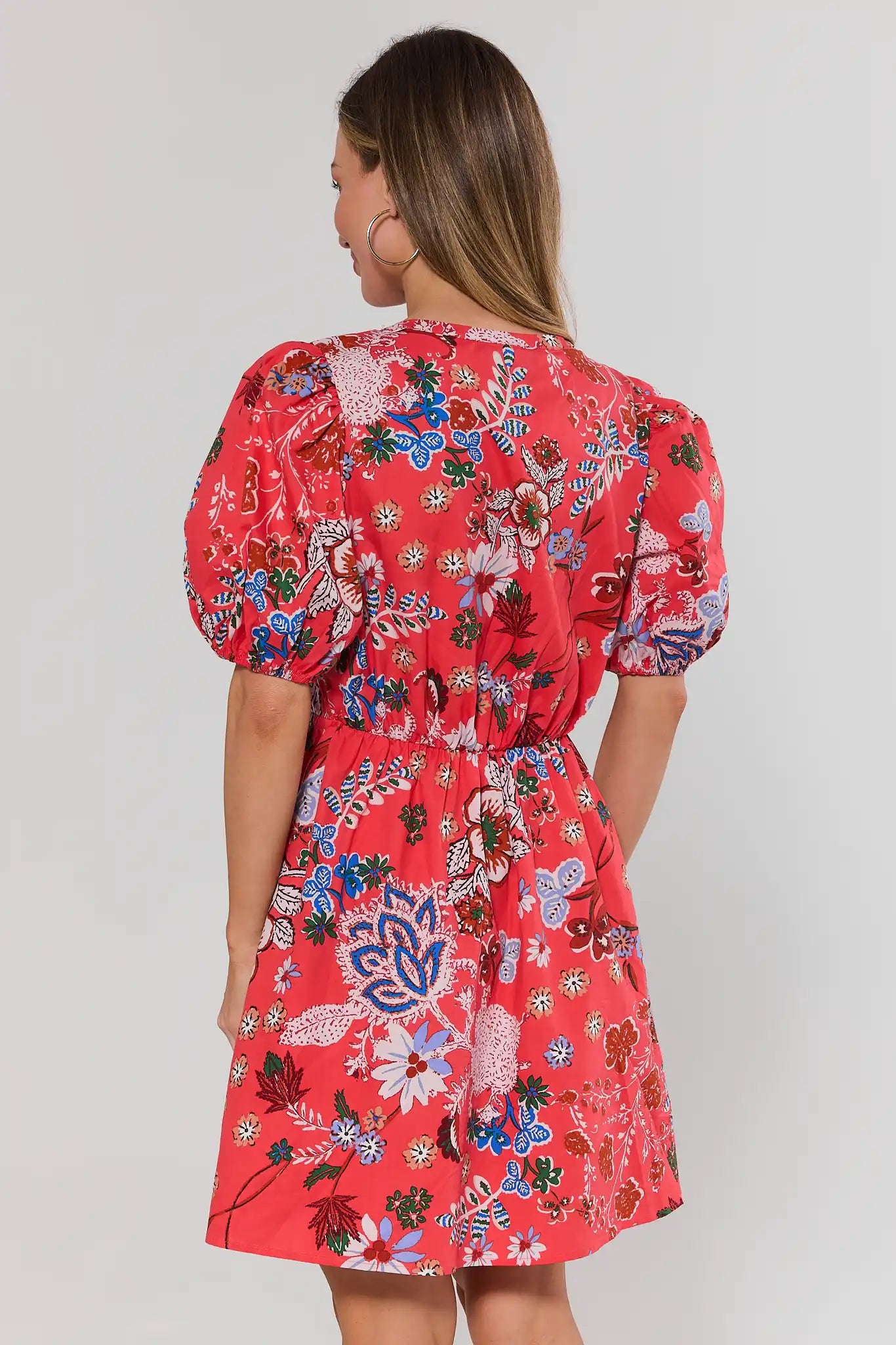 Woman wearing a coral floral dress against a plain background standing