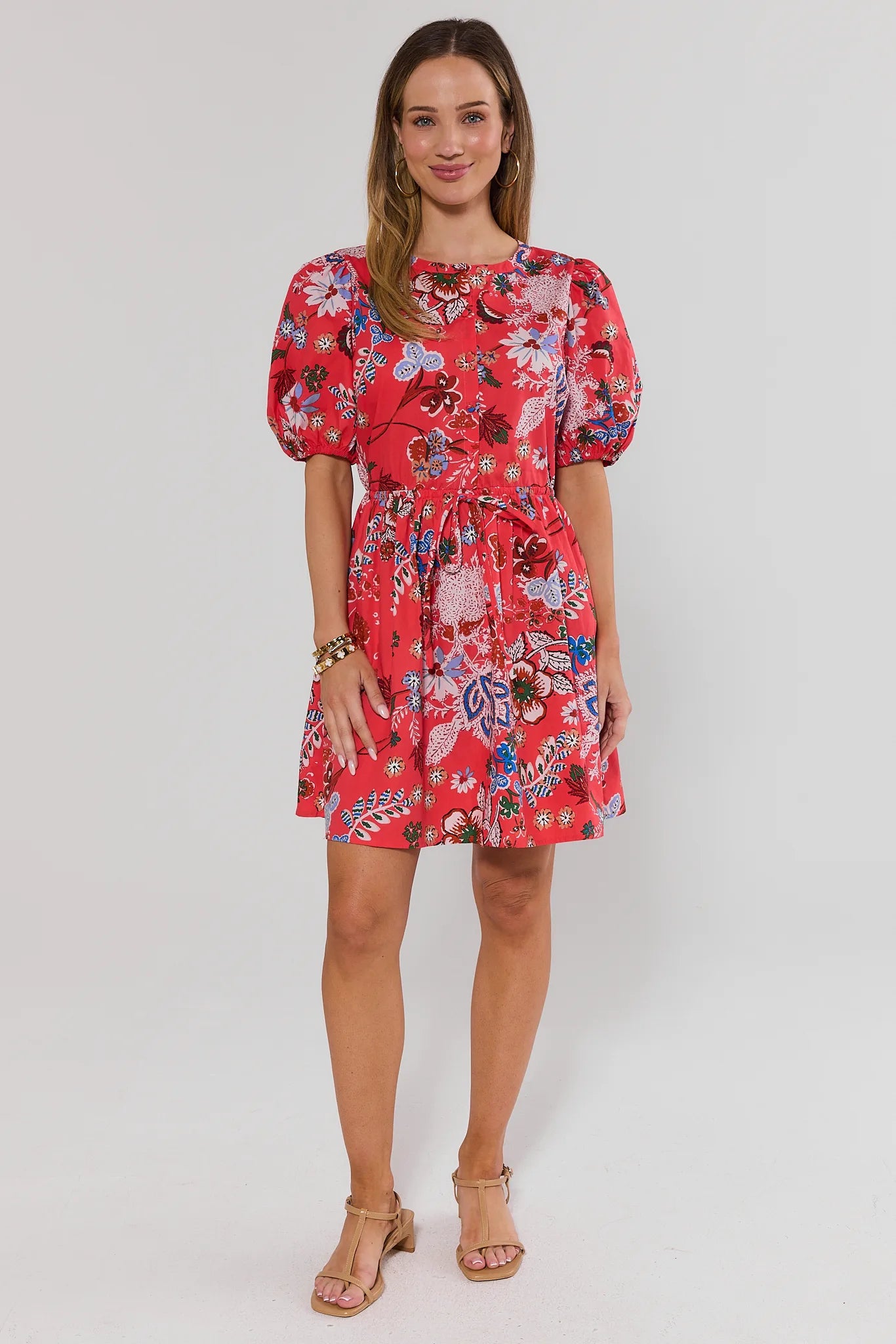 Woman wearing a coral floral dress on a white background stand
