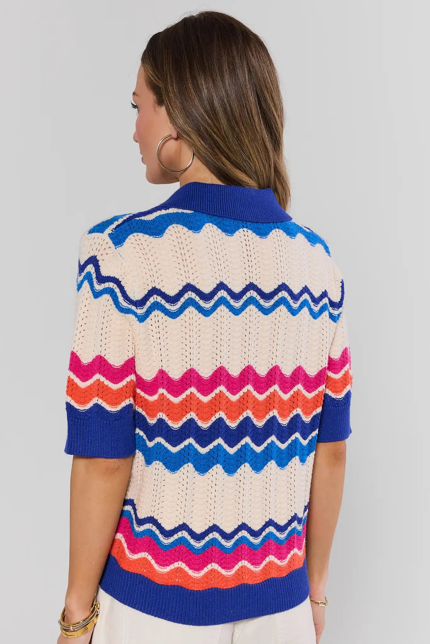 Woman wearing a colorful striped sweater on a plain background stand