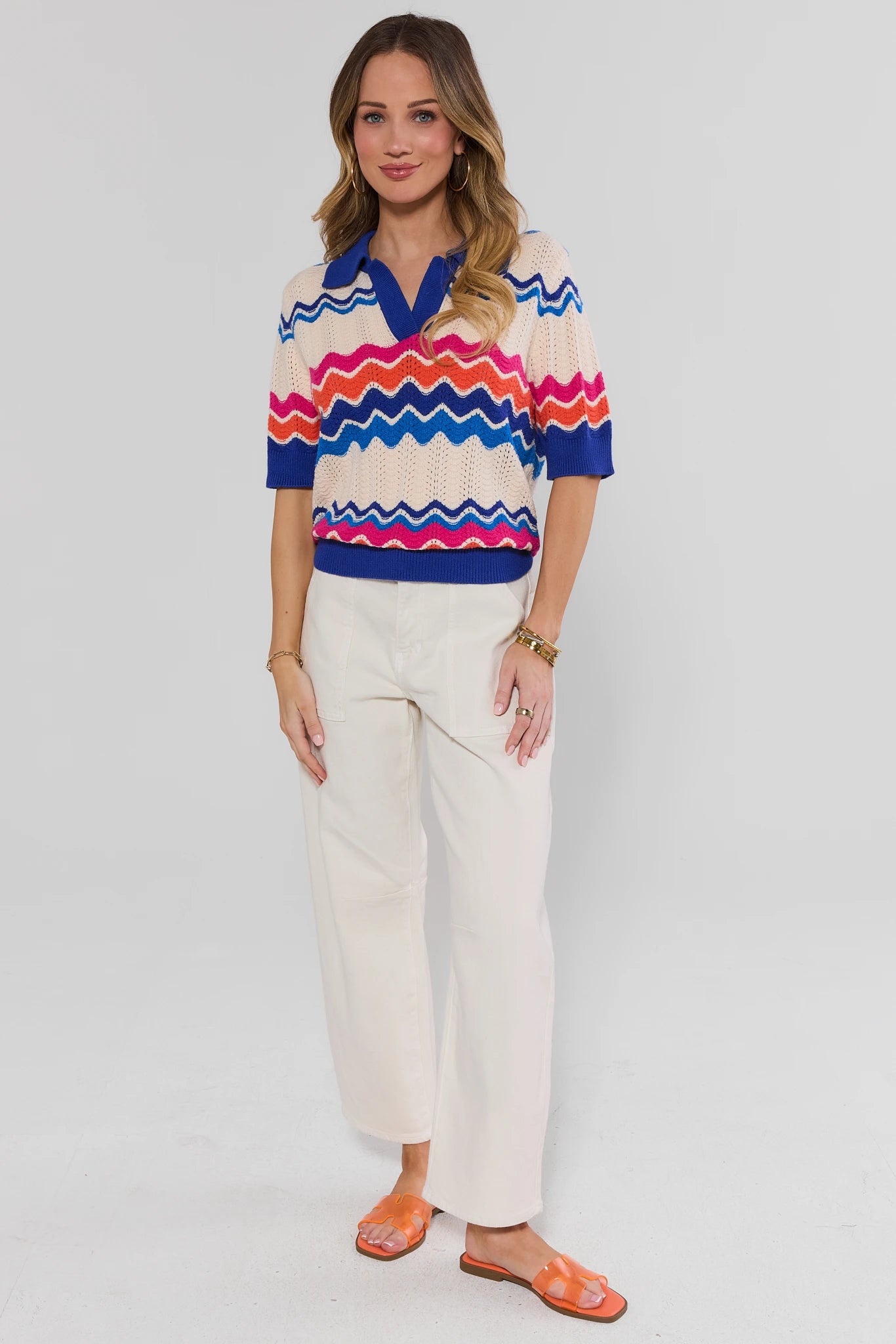 Woman wearing a colorful striped shirt and white pants on a gray background