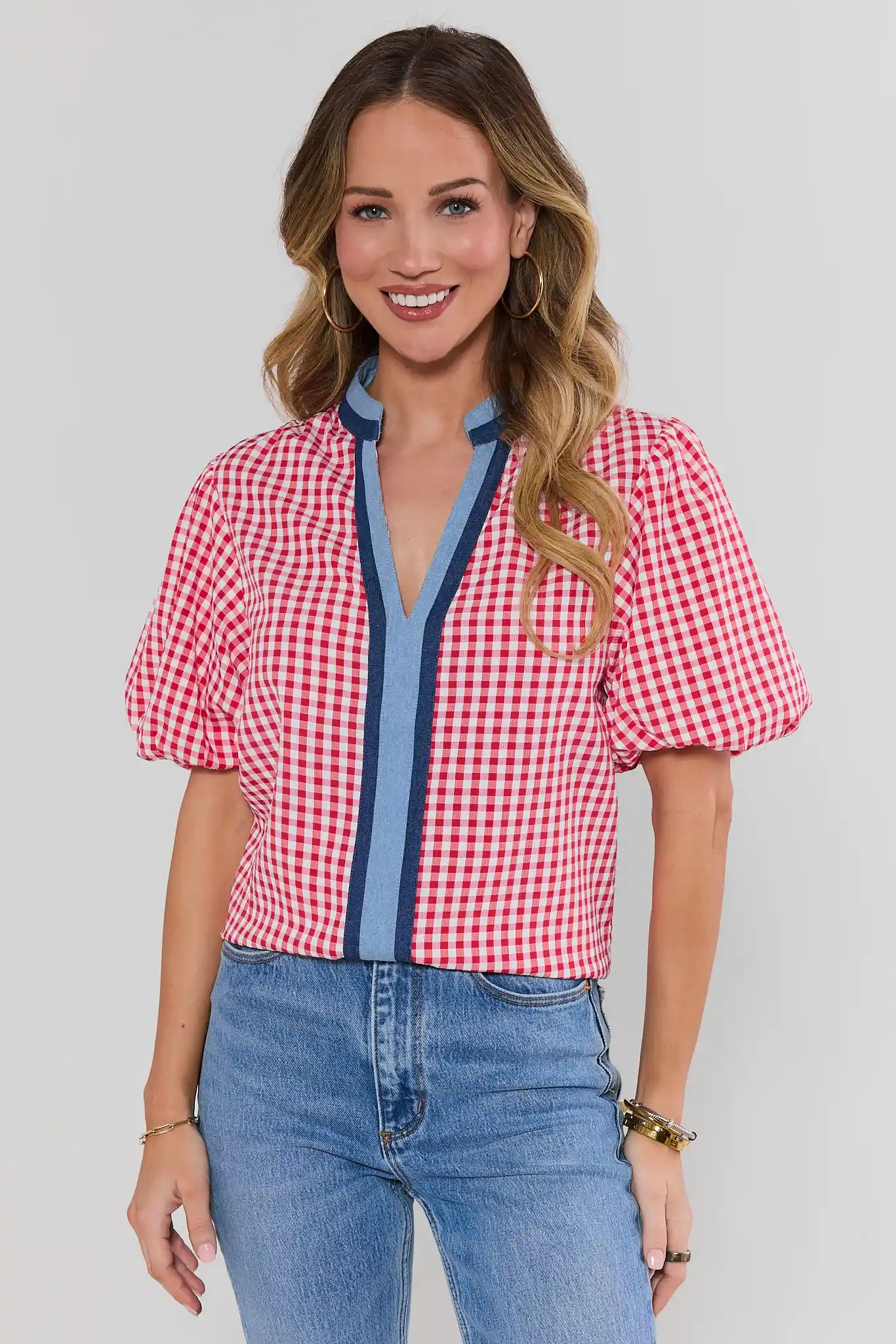 Woman wearing a red and white checkered shirt with blue accents and blue jeans on a plain background